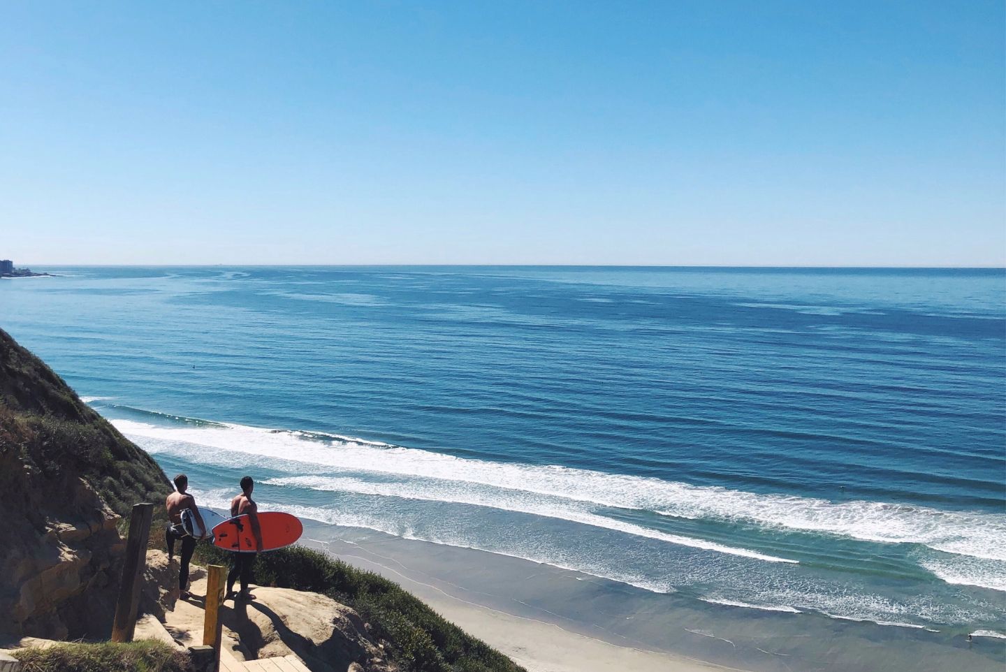 Two surfers looking over the cliffside of Black's Beach California looking out onto the blue oceans