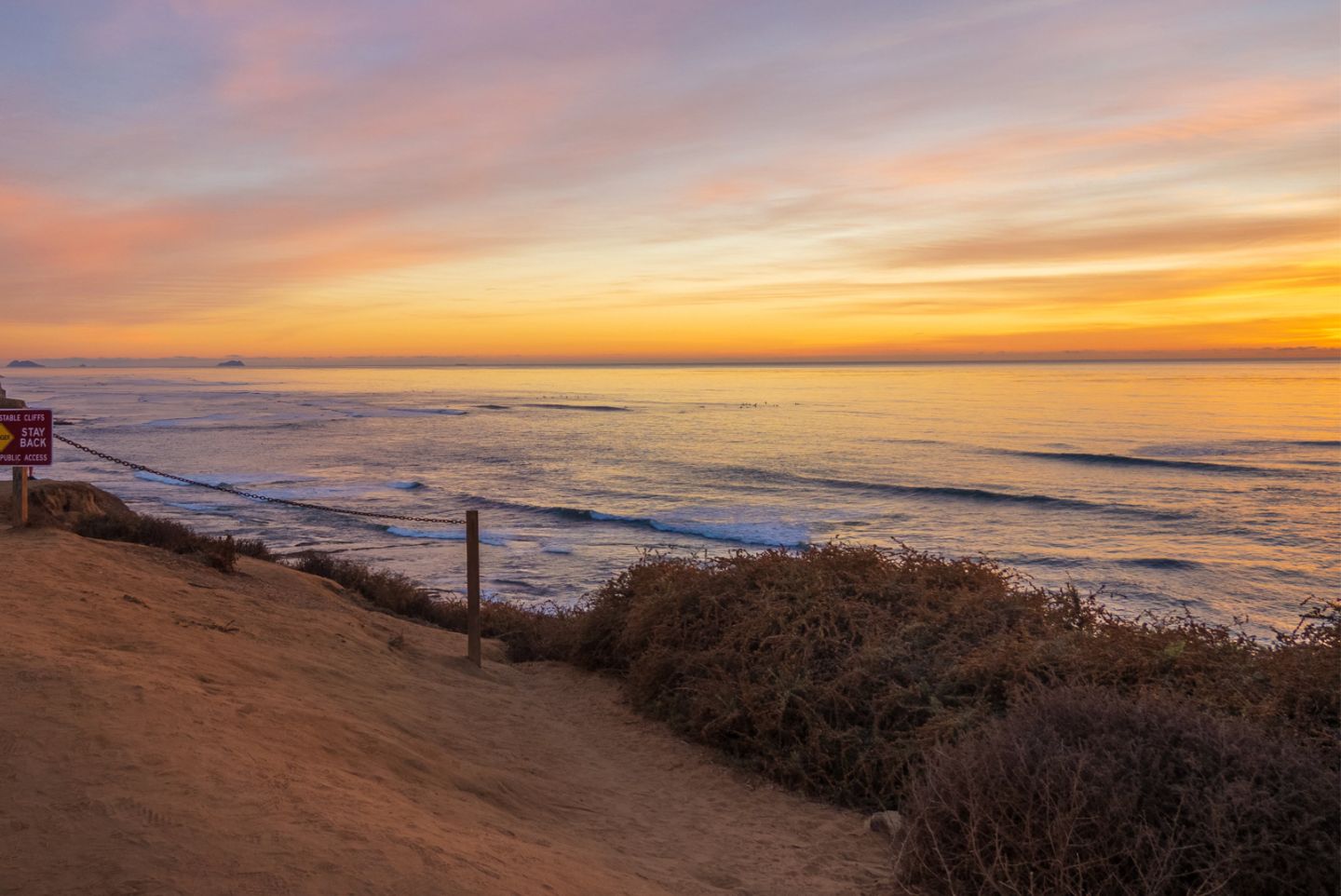 on the cliffside of sunset cliffs with an orange and pink sunset on the horizon 