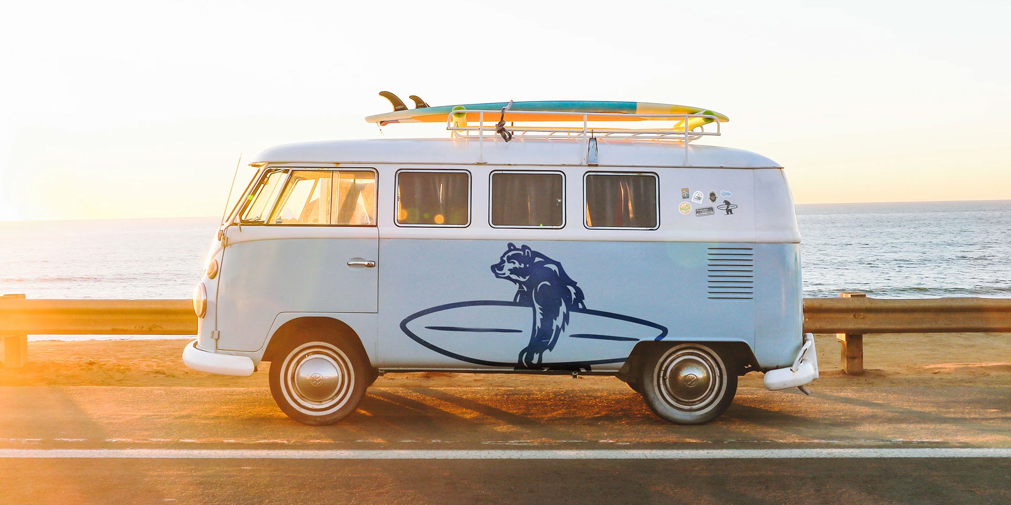 Photo of a VW van with Brutus the Bear graphic logo on it. The van is sitting in front of the ocean.
