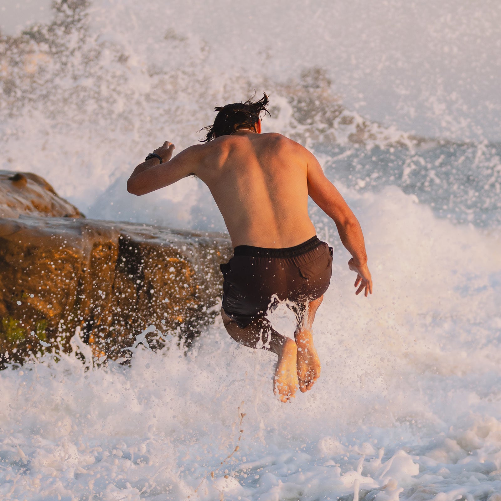 Man jumping into ocean waves wearing Everyday California brown boardshorts with black trim