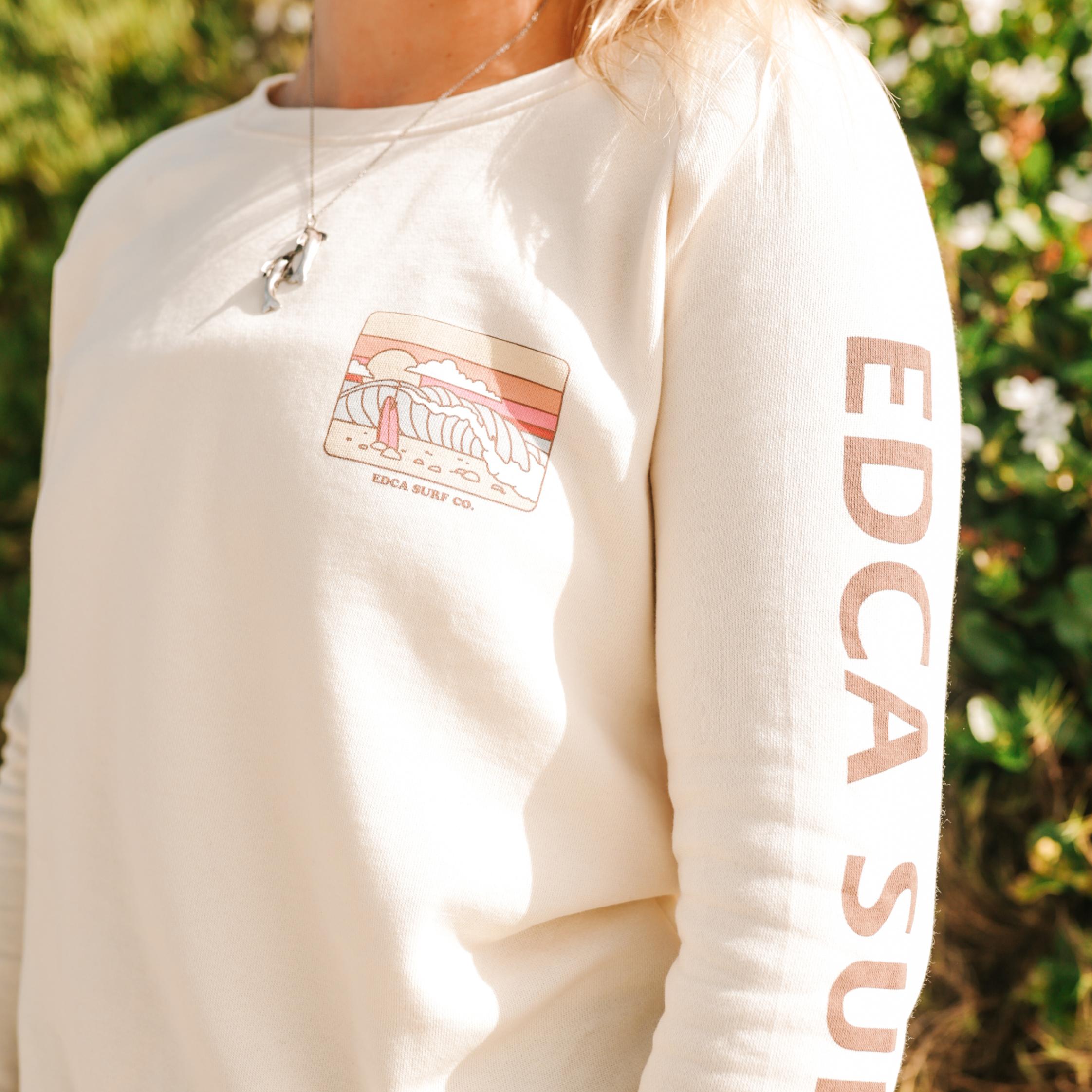 White sweatshirt with a logo and text on sleeves against a blurred green background