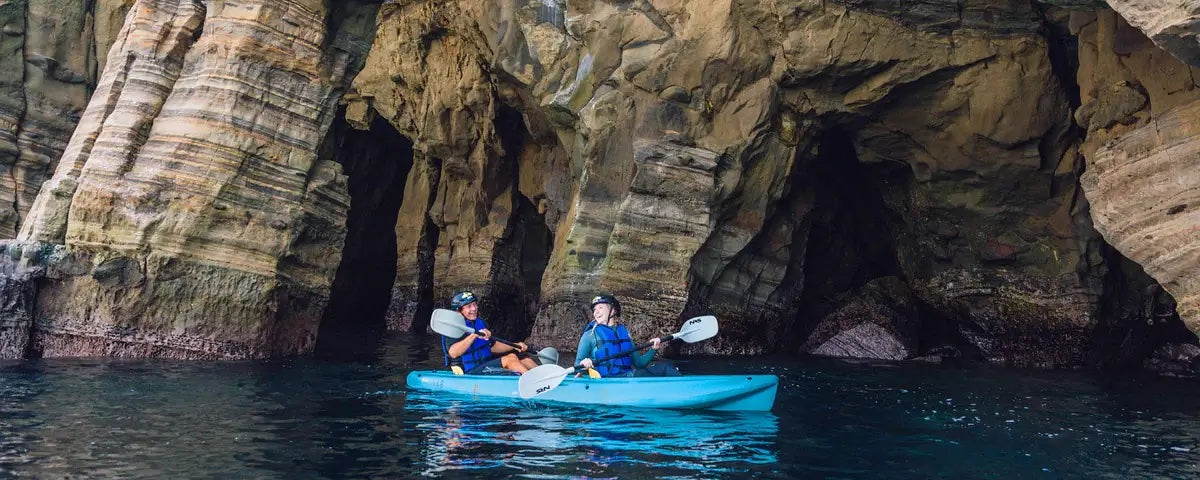 Two kayakers on a Sea Cave Kayak Tour with Everyday California, sitting in a kayak in the ocean in La Jolla right in front of the entrance to one of the Seven Sea Caves.