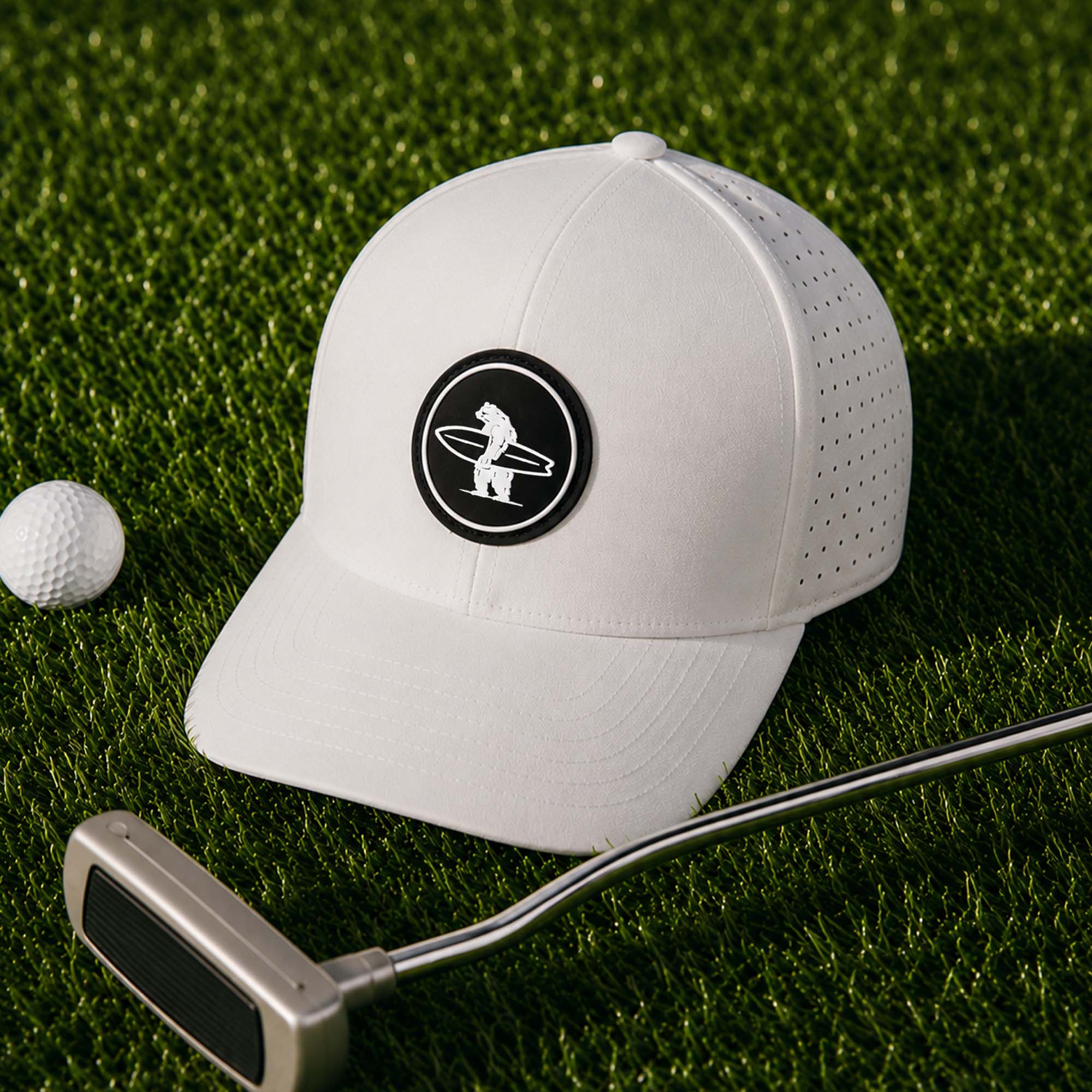 White golf cap with a logo on a green grass background, next to a golf ball and putter.