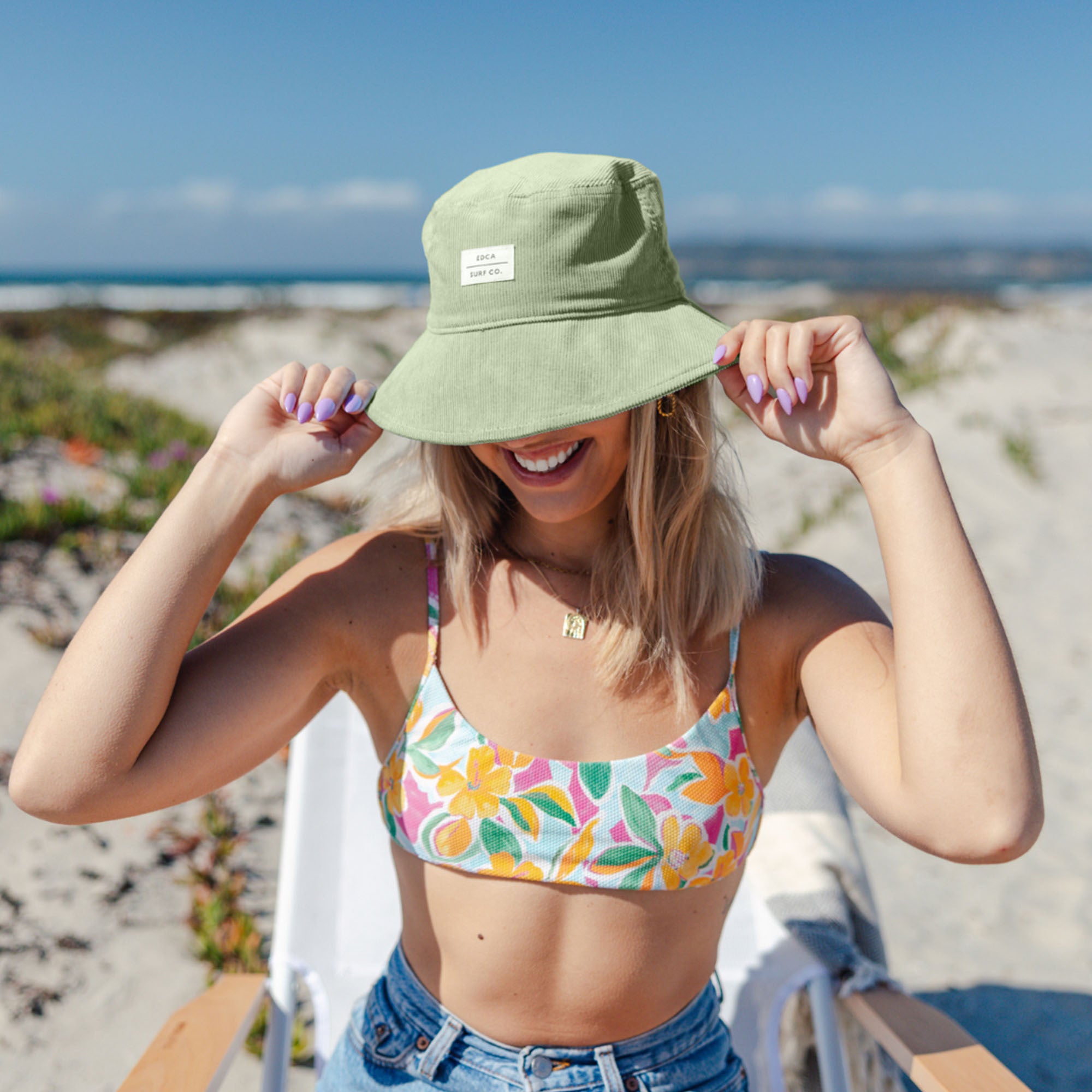 Woman wearing a floral bikini top and green bucket hat on a beach.