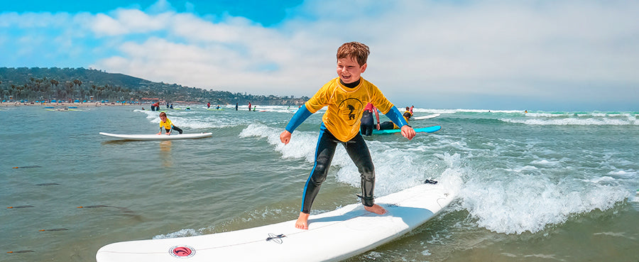 Child standing on surfboard amid the Kids Surf Camp