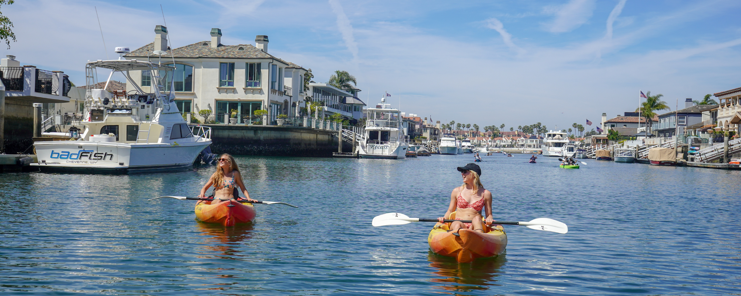 Two girls kayaking through the Huntington Beach Harbour. The calm waters are perfect for exploring around the yachts and beautiful houses on the water.