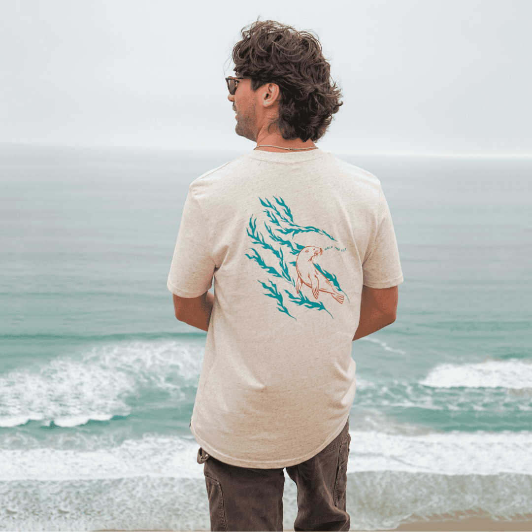 Man wearing a beige t-shirt with a graphic design standing on a beach.