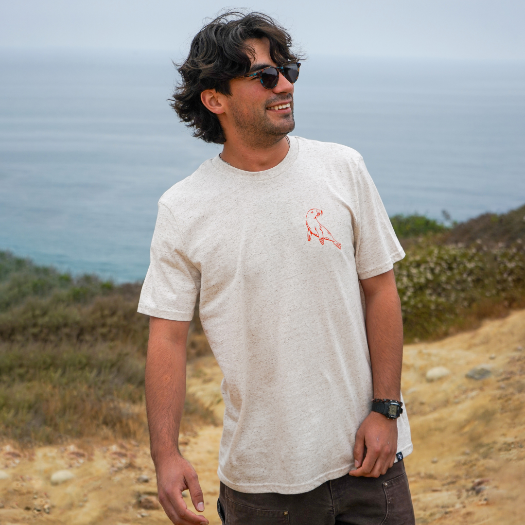 Man wearing a white t-shirt with a logo standing on a dirt path with ocean view