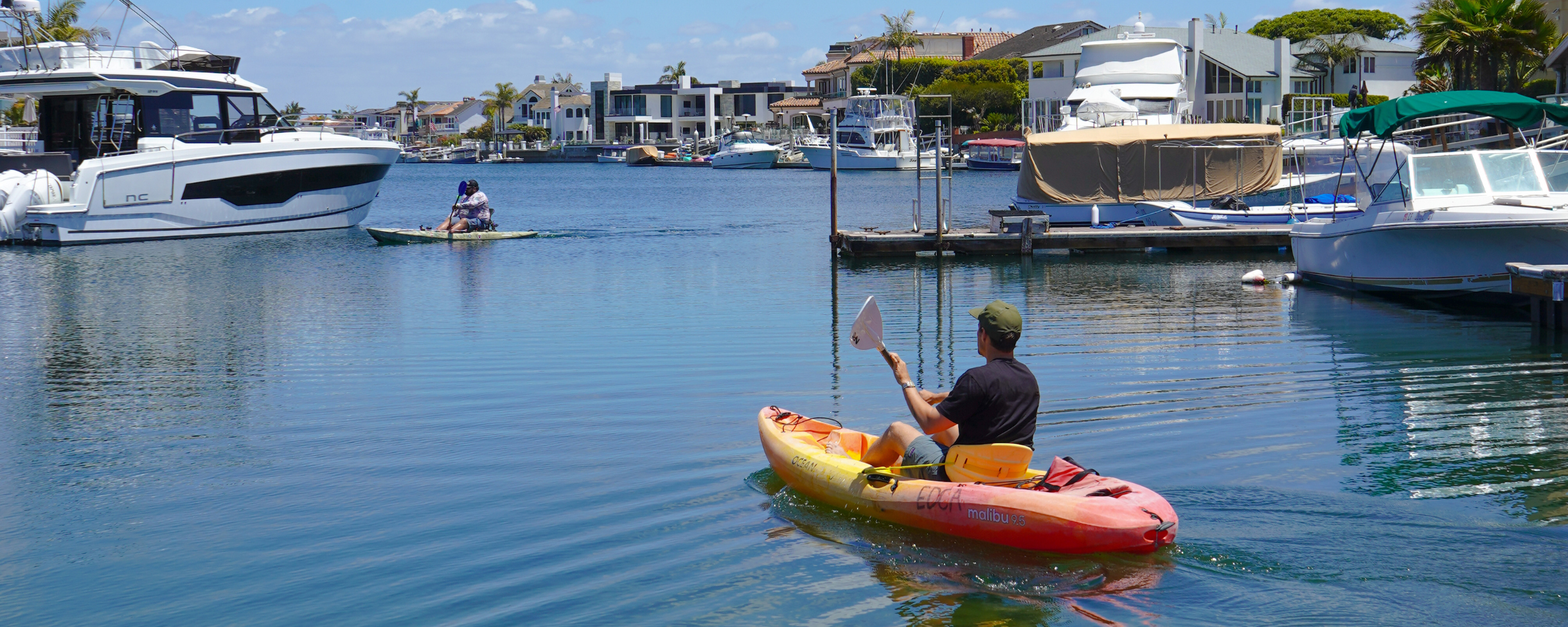 Two kayakers paddling through the calm waters of the Huntington Harbour canals near Huntington Beach, California.