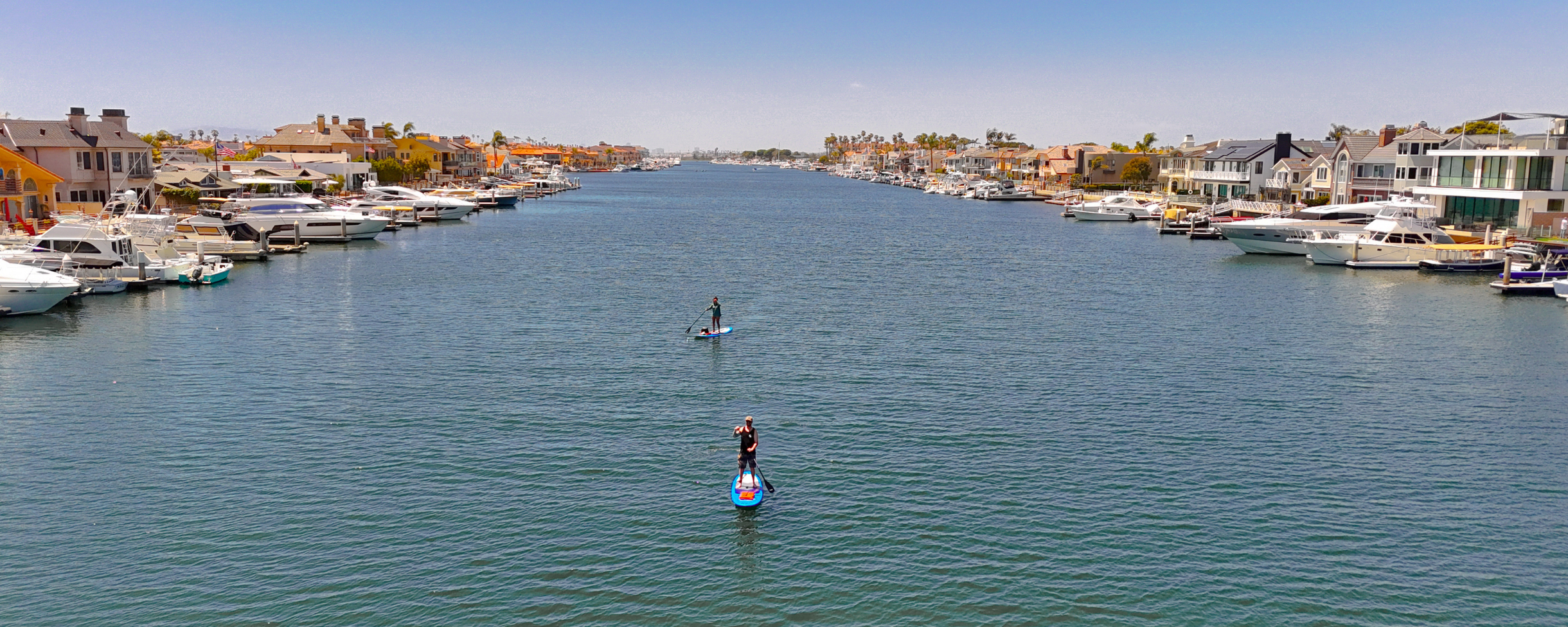 Two stand up paddle boarders paddling through the calm waters of Huntington Harbour in Sunset Beach, California.