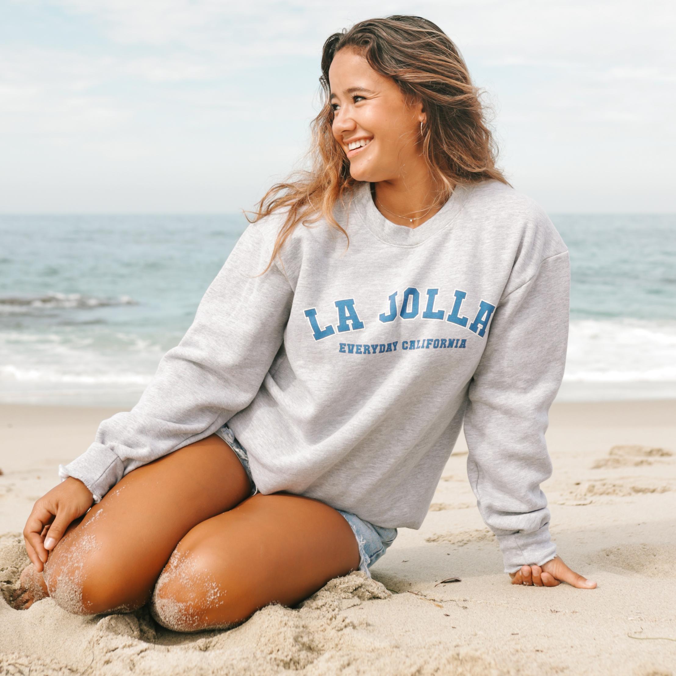 Girl on the beach wearing a grey crewneck that says La Jolla Everyday California