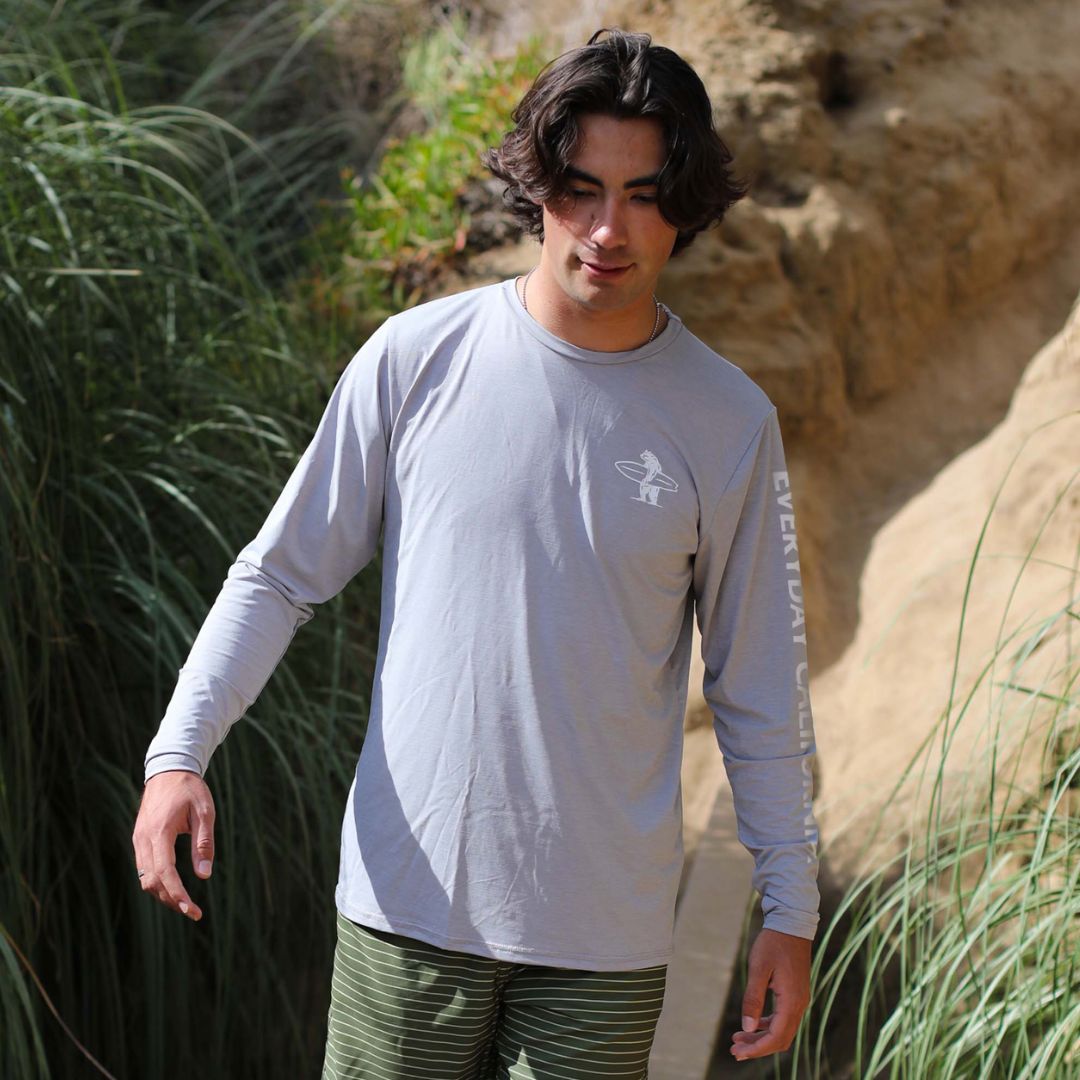 A California man wearing a light grey rash guard walking down a hiking trail