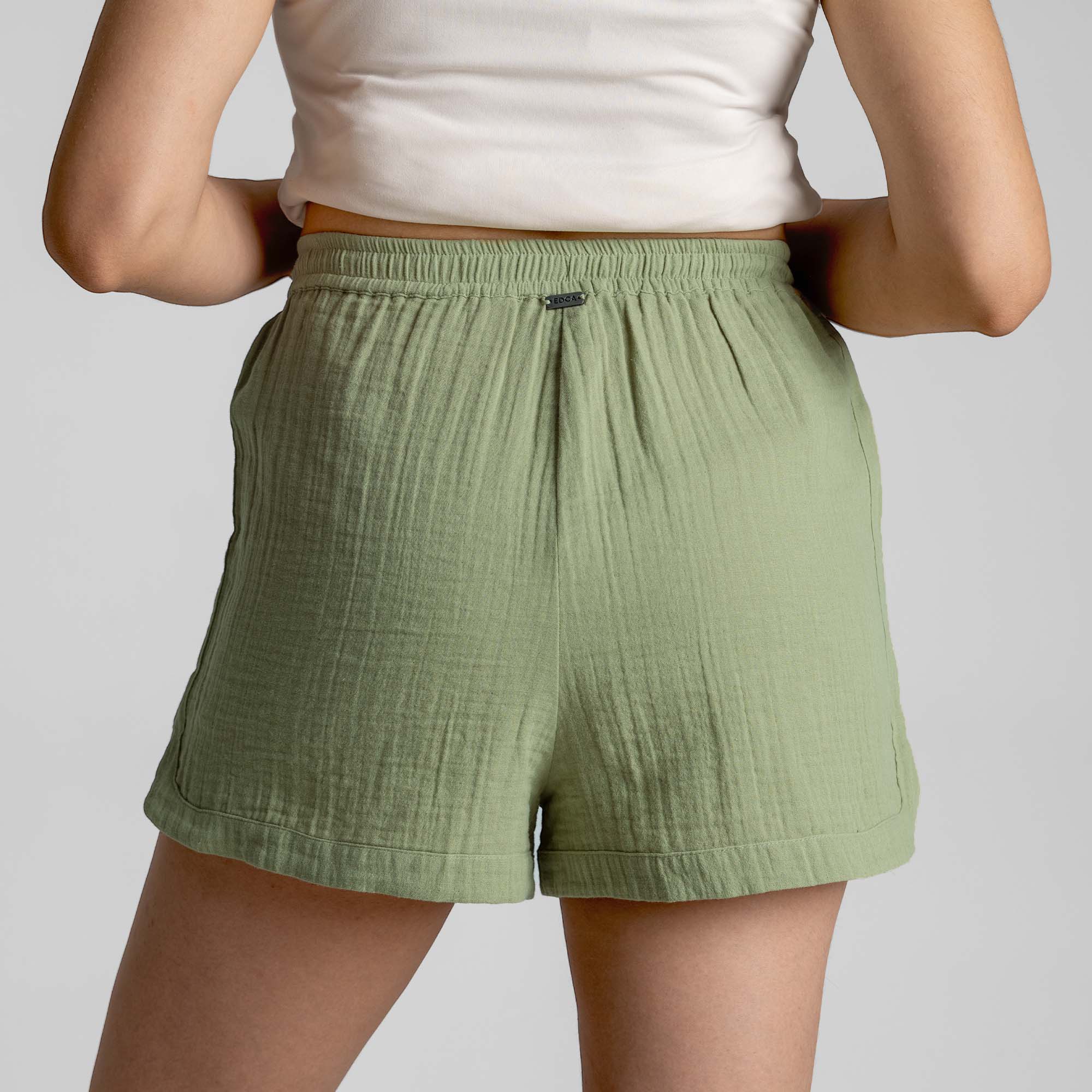 Person wearing green shorts and a white top on a plain background