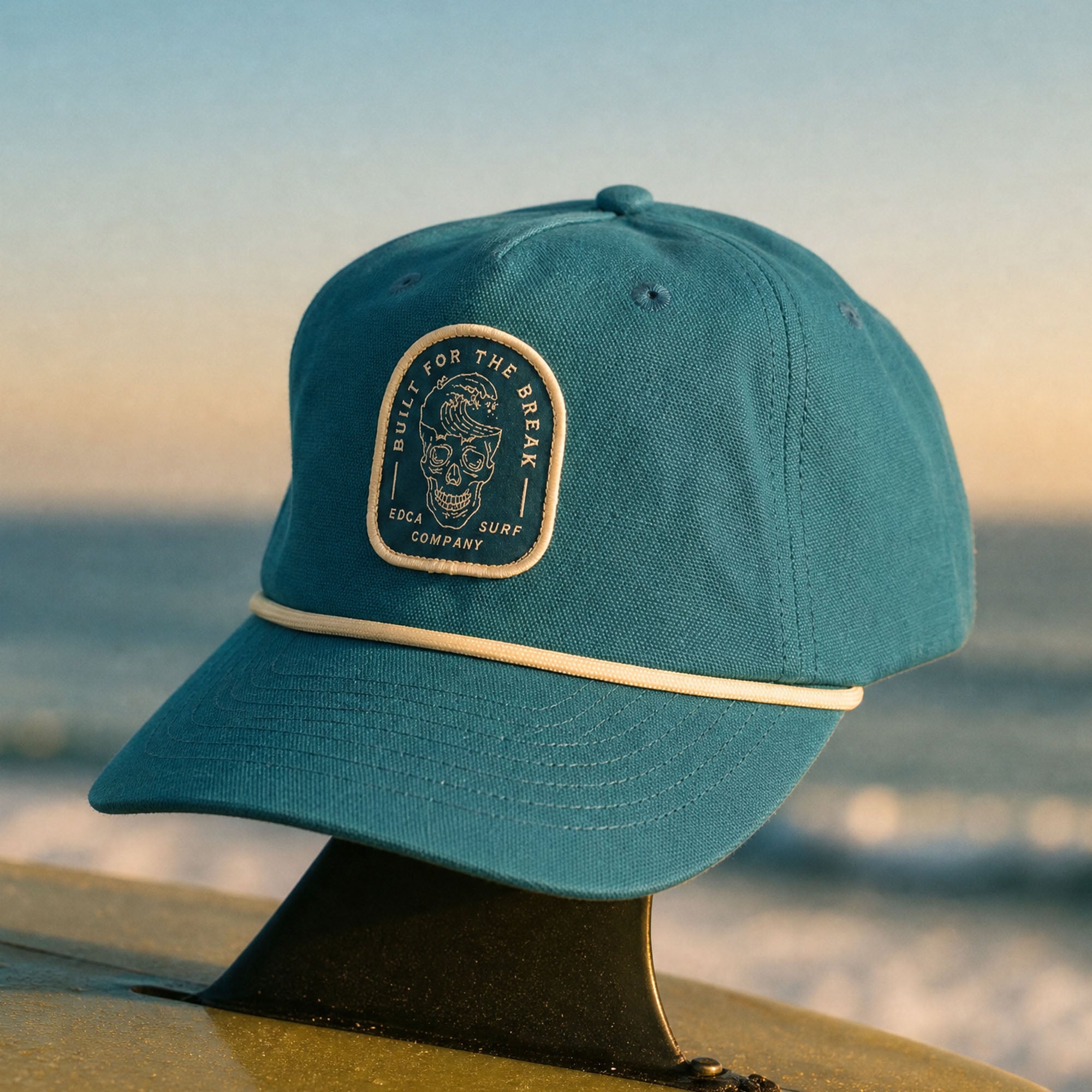 Cotton hemp canvas snapback hat in the color blue. Patch on the front with a white outline of a skull where the top of the skull is a wave. White cord across the brim.