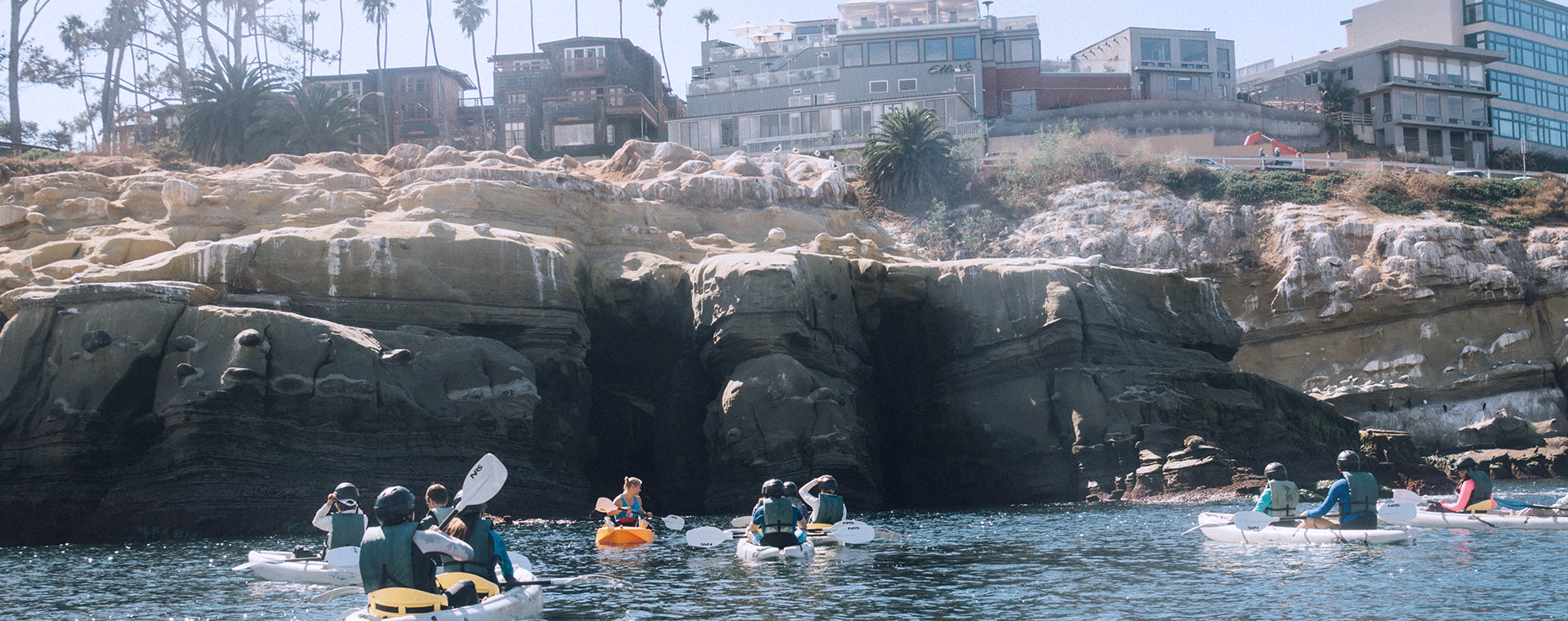A group of 20 people on a private group kayak tour in front of the Seven Sea Caves in San Diego with Everyday California tour guides.