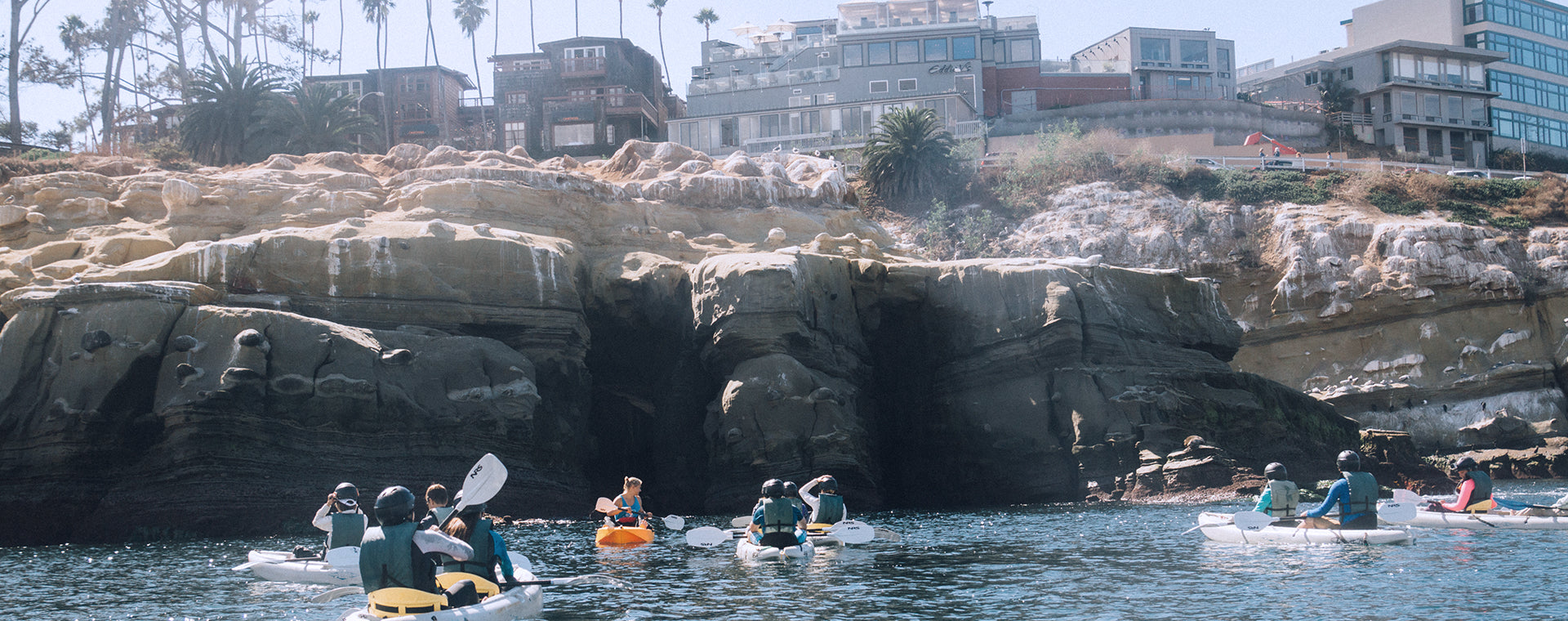 A group of 20 people on a private group kayak tour in front of the Seven Sea Caves in San Diego with Everyday California tour guides. 