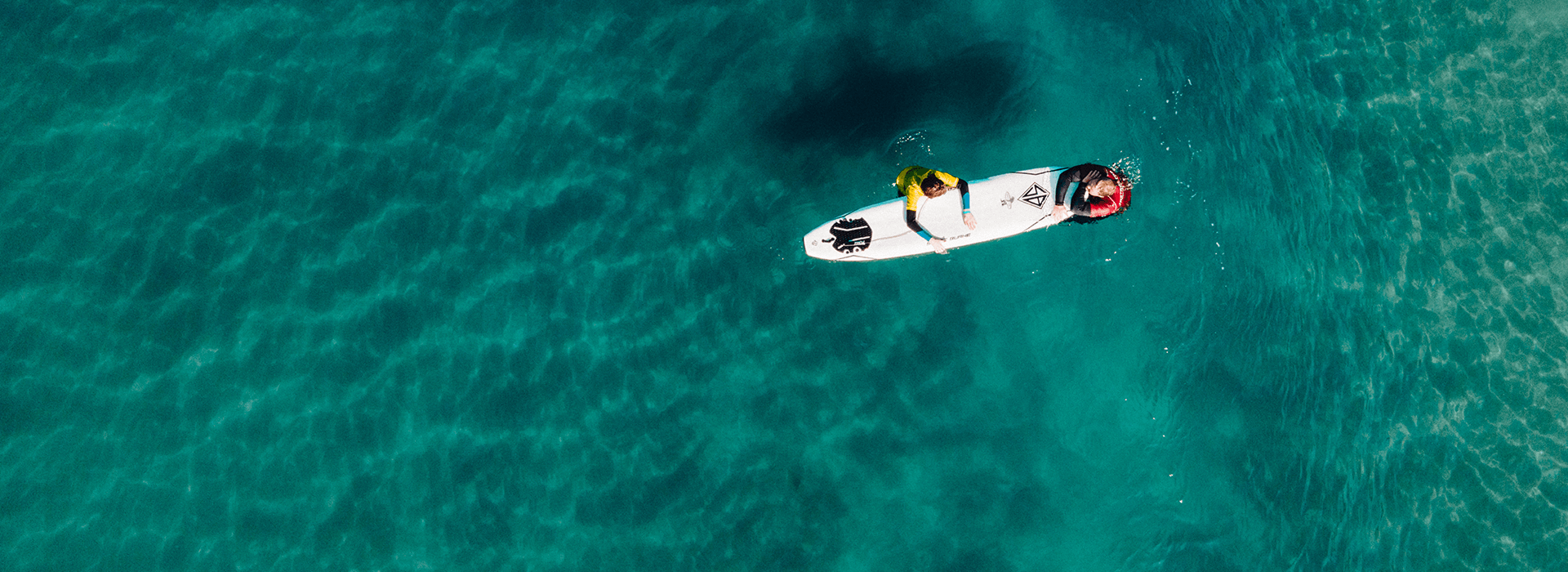 Drone overview of a camp counselor on a surfboard with a child in surf camp with Everyday California in La Jolla