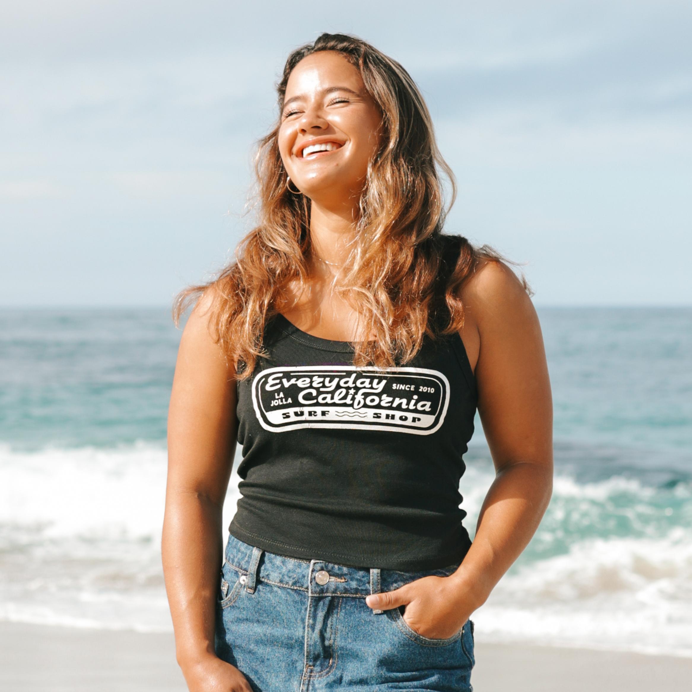 Woman wearing a black tank top with 'Everyday California' logo on a beach