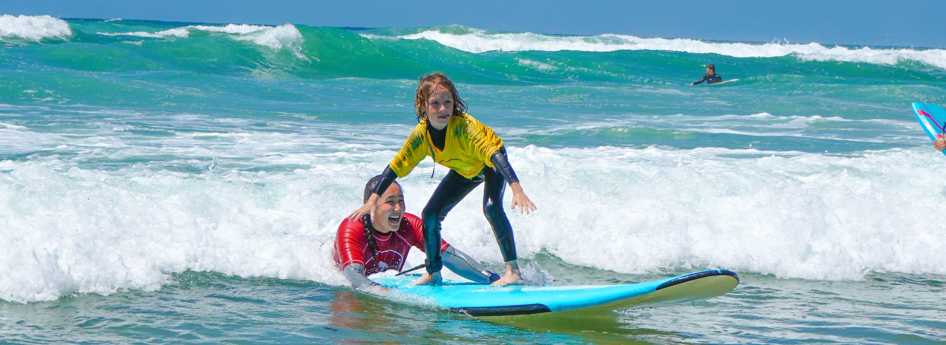 Surf student pops up on a wave, gets pushed into surf by Everyday California surf camp instructor