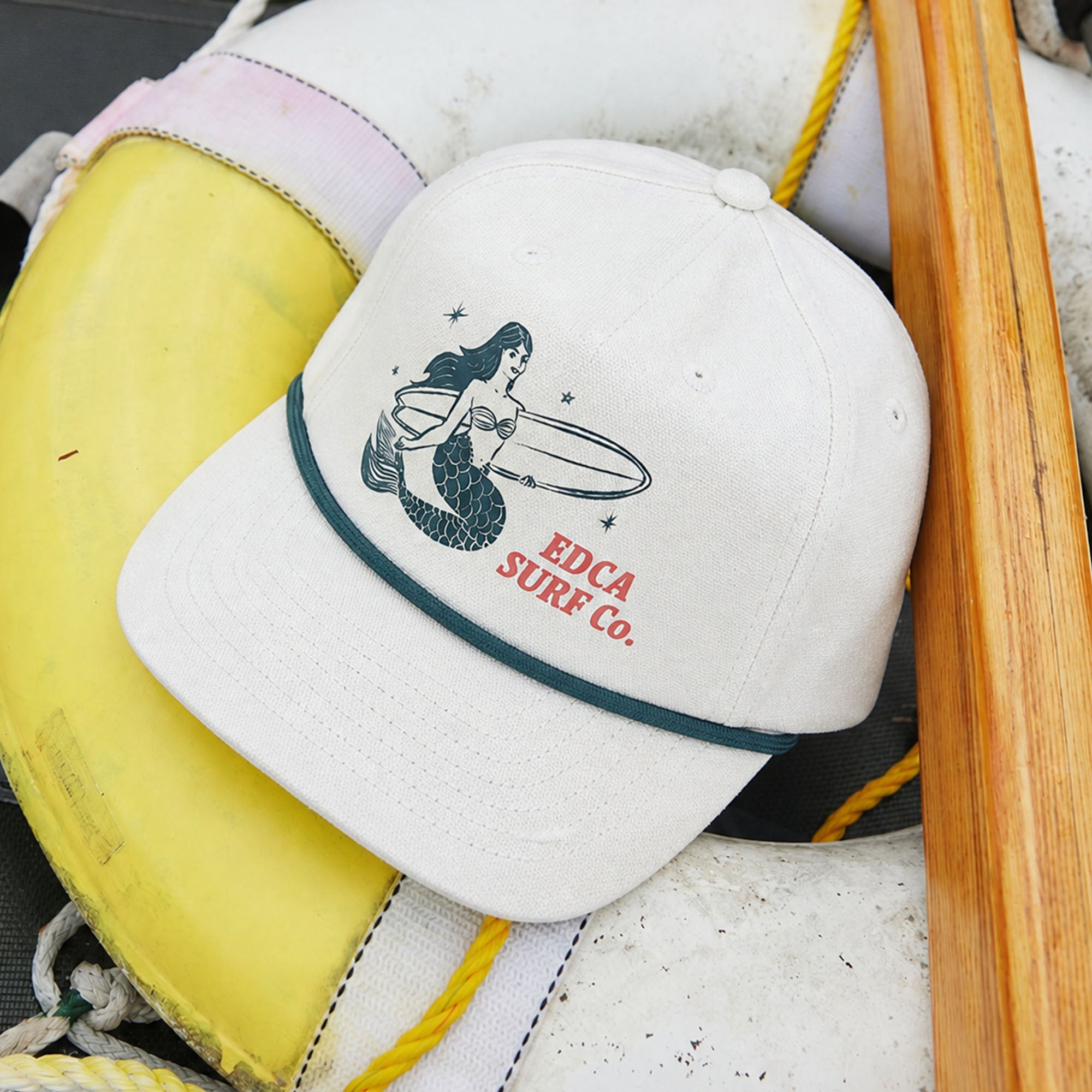 Cotton Hemp canvas snapback hat with a screen printed image of a blue mermaid holding a surfboard on the front, with red text next to the mermaid that reads 'EDCA SURF CO.'.