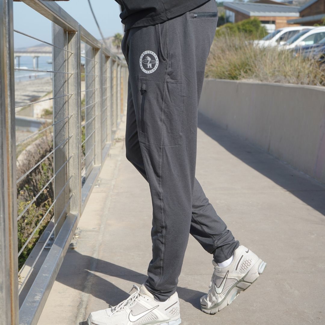 Man modeling the black Bayside Performance joggers featuring a small reflective vinyl logo near the hip pocket of a bear holding a surfboard.