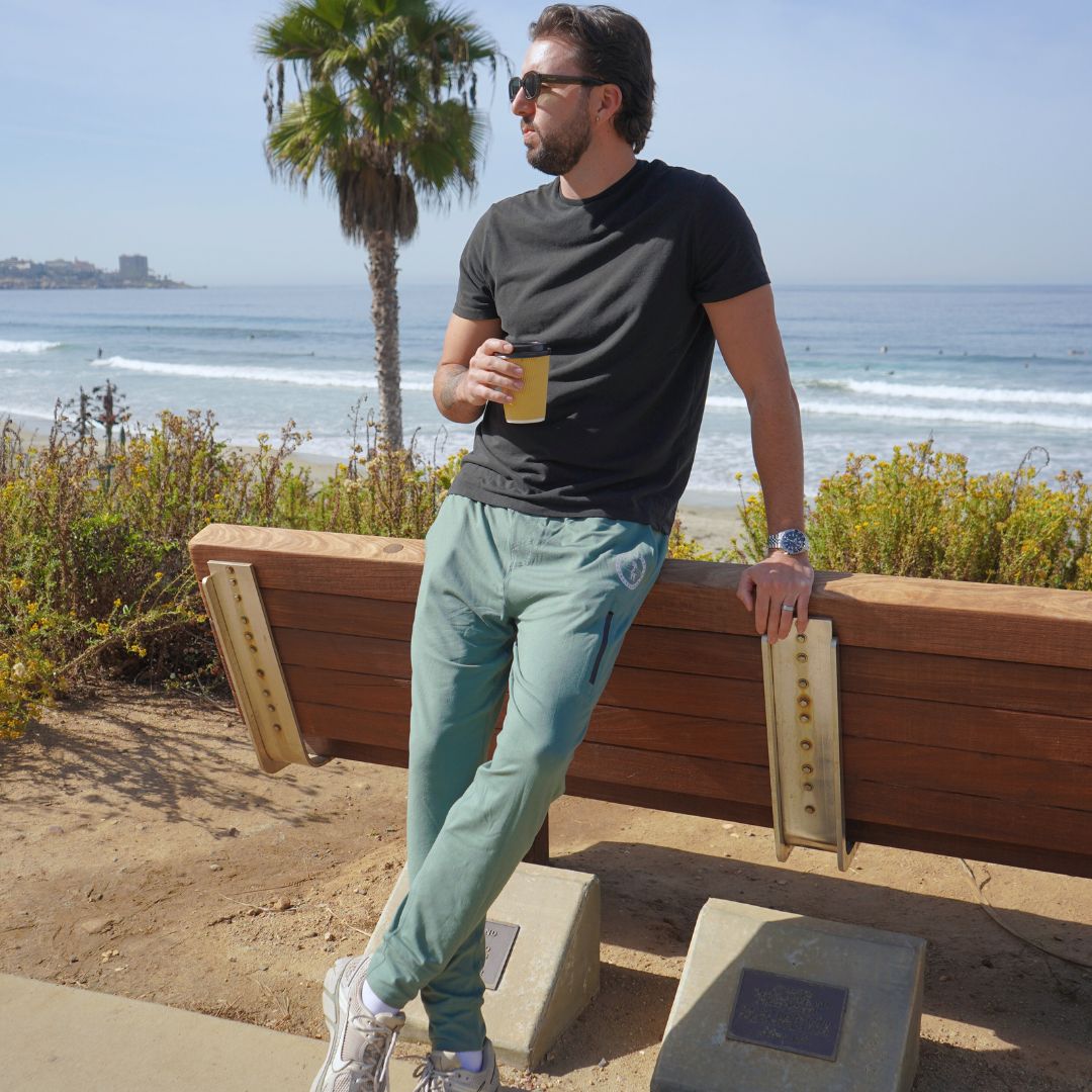 Man modeling the green Bayside Performance joggers featuring a small reflective vinyl logo near the hip pocket of a bear holding a surfboard.