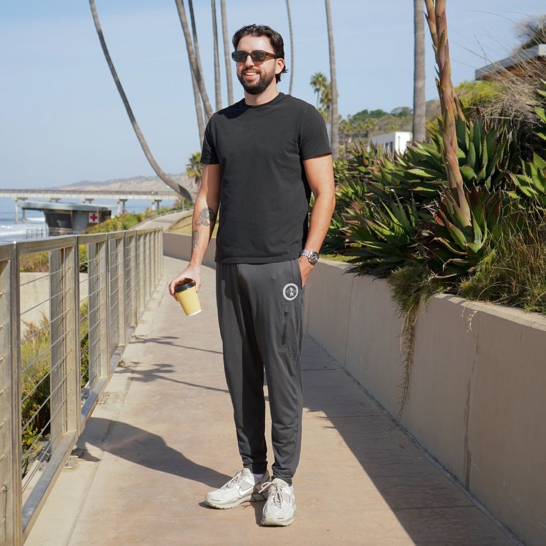 Man modeling the black Bayside Performance joggers featuring a small reflective vinyl logo near the hip pocket of a bear holding a surfboard.