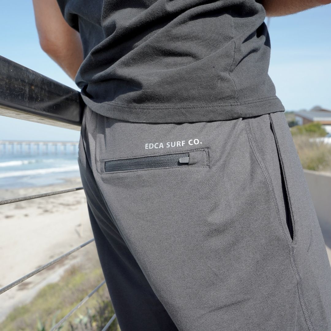 Man modeling the black Bayside Performance joggers featuring a small reflective vinyl logo near the back pocket of the words 'EDCA SURF CO.'