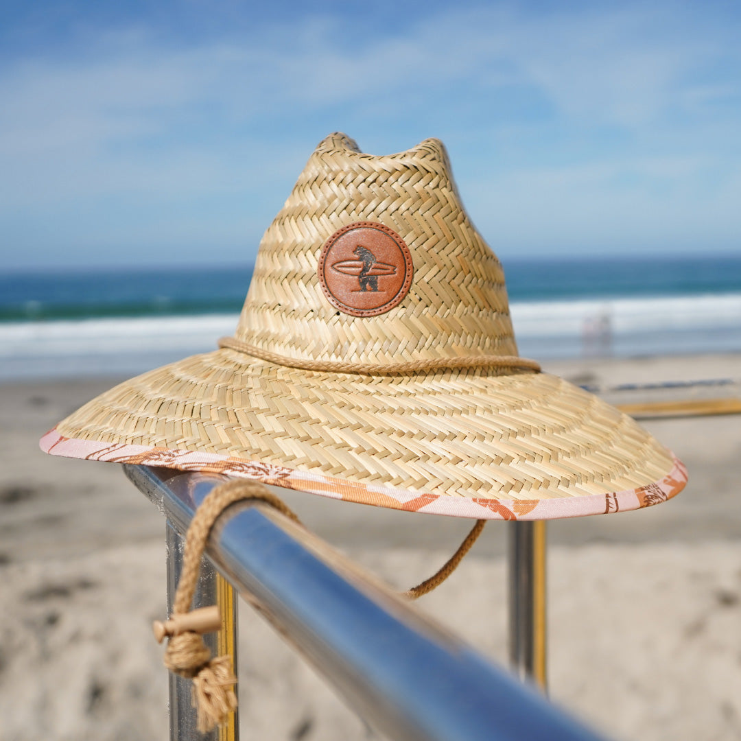 A beige Eddie Straw Hat with a wide brim and a logo patch on the crown, featuring a natural straw weave and an adjustable chin strap.