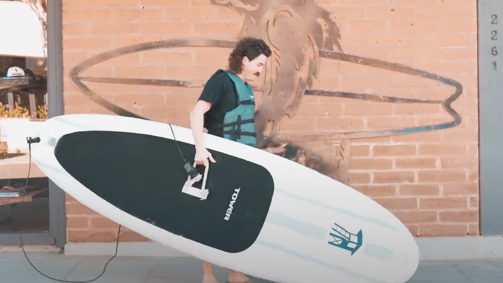 Photo of a man carrying a stand up paddle board down a sidewalk