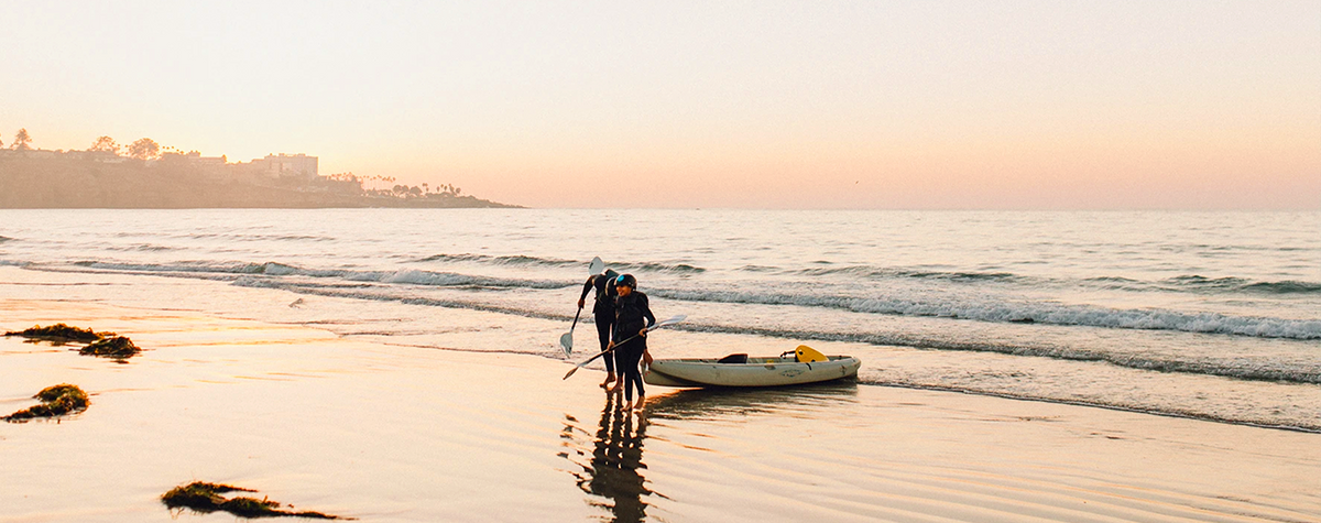 Two EDCA kayak renters in La Jolla pulling up a tandem kayak with the waves crashing in the background.