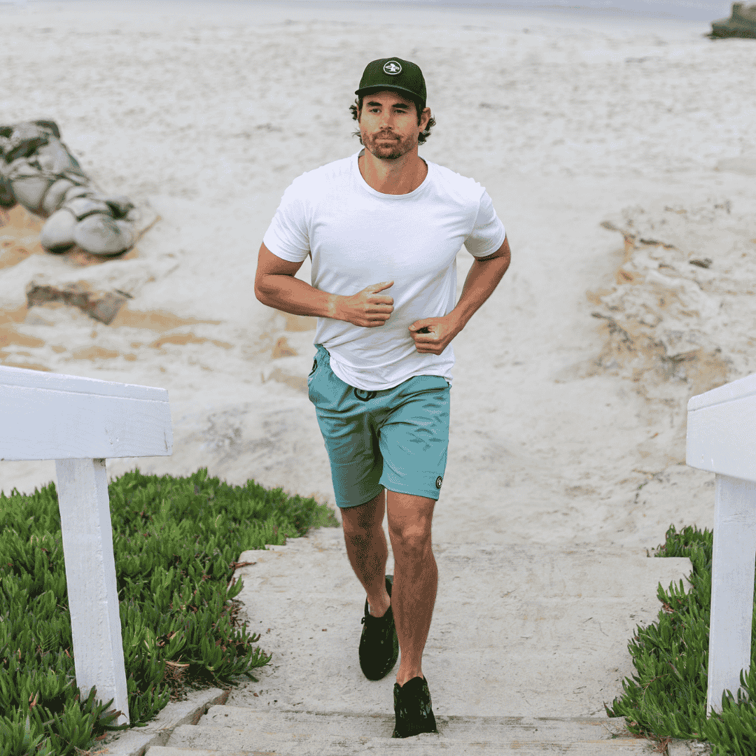 Male model running up stairs at the beach wearing Everyday California hat and shorts