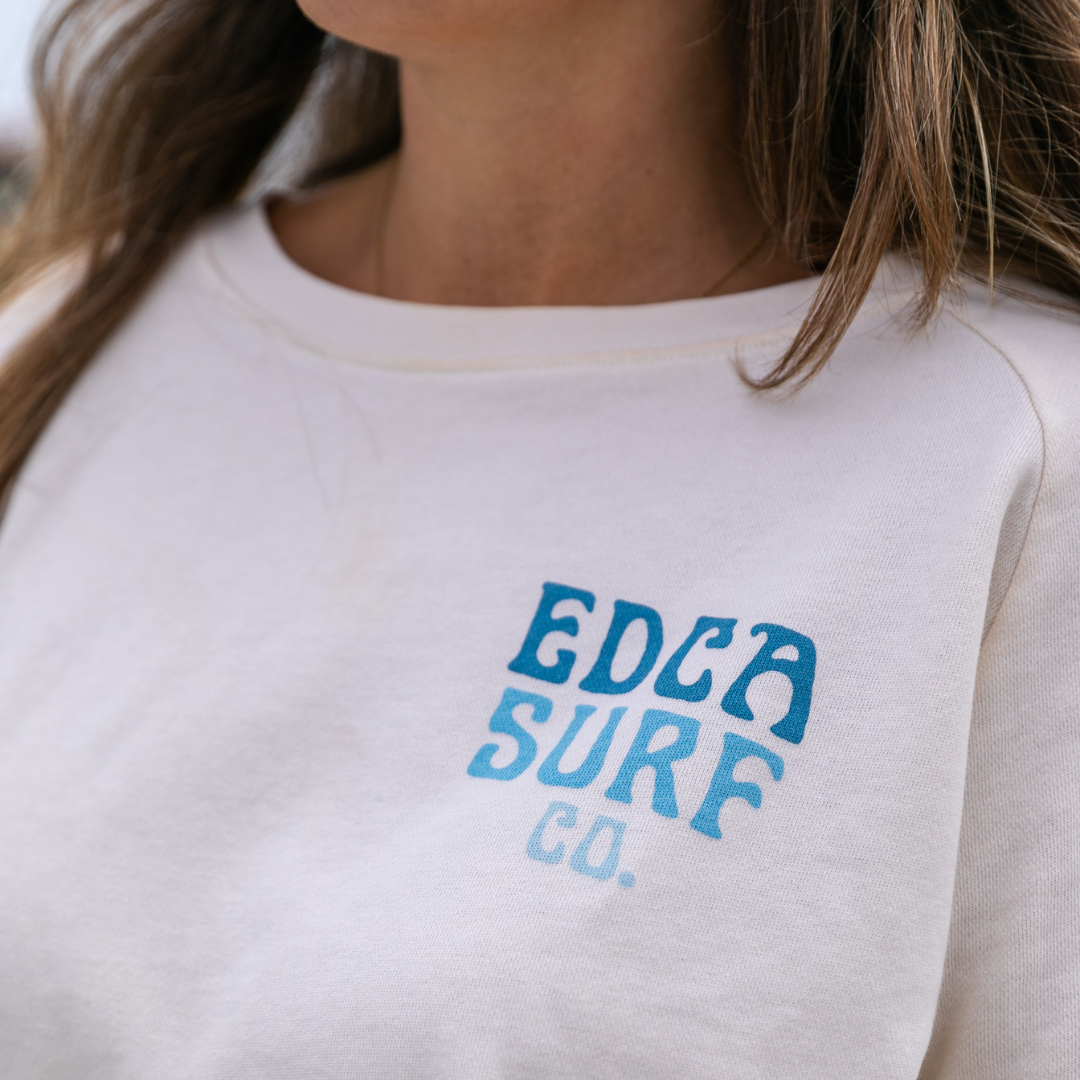 Closeup of female model wearing white Everyday California crewneck with "EDCA Surf Co." logo in blue