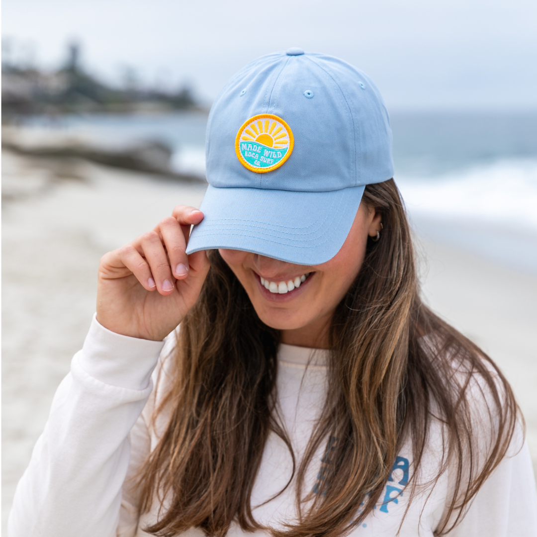 Closeup of female model with brown hair wearing a light blue Everyday California hat with a logo that reads "Made Wild. EDCA Surf Co."