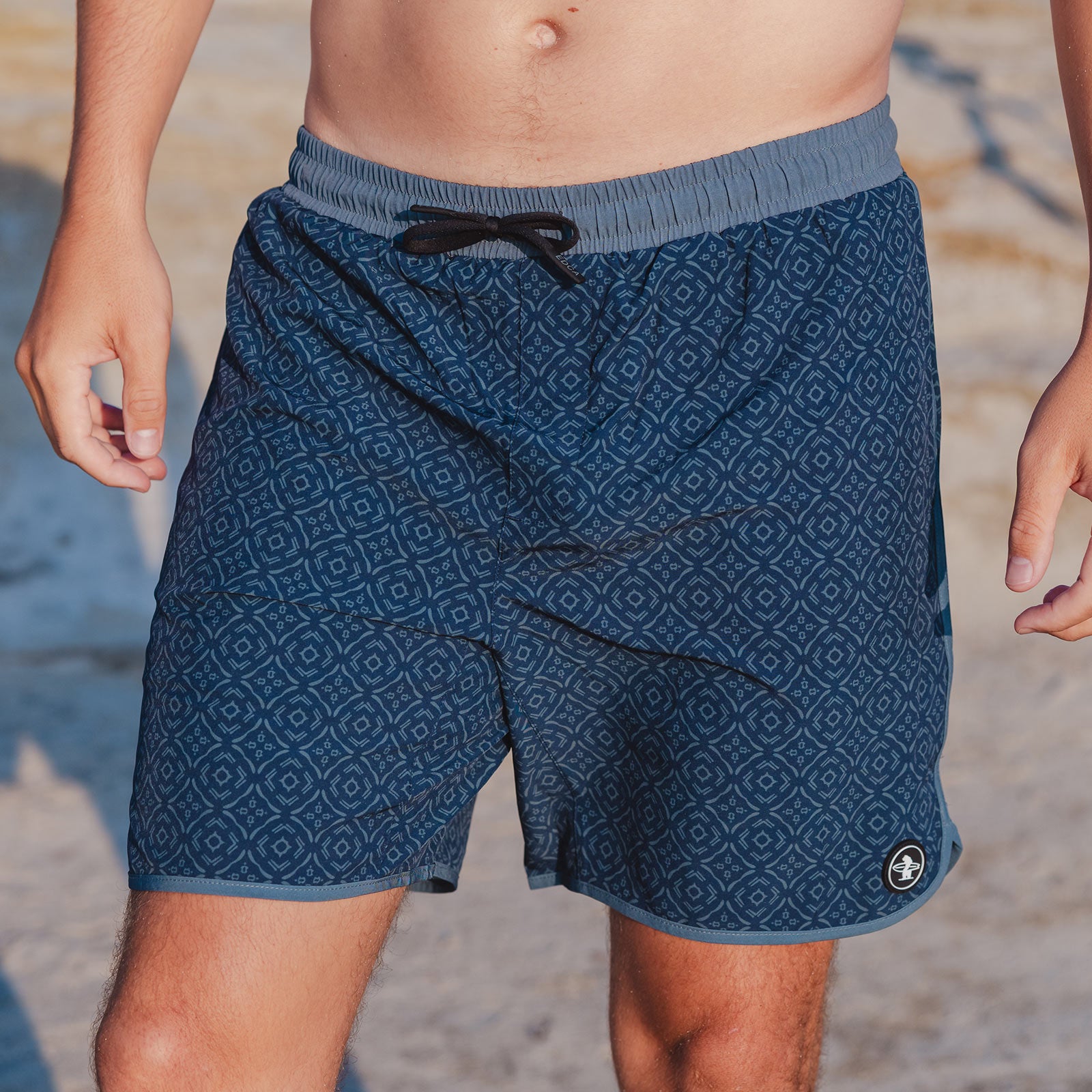 Blue patterned Everyday California shorts worn by a person on a beach.