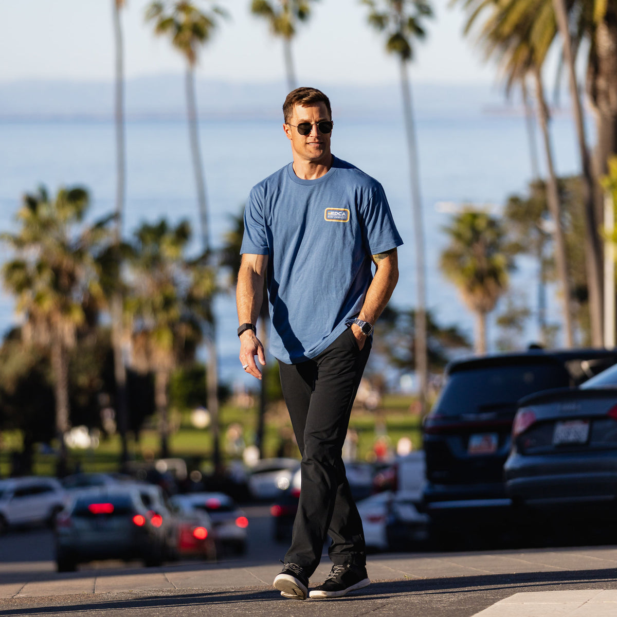 Man walking on a street with palm trees and cars in the background