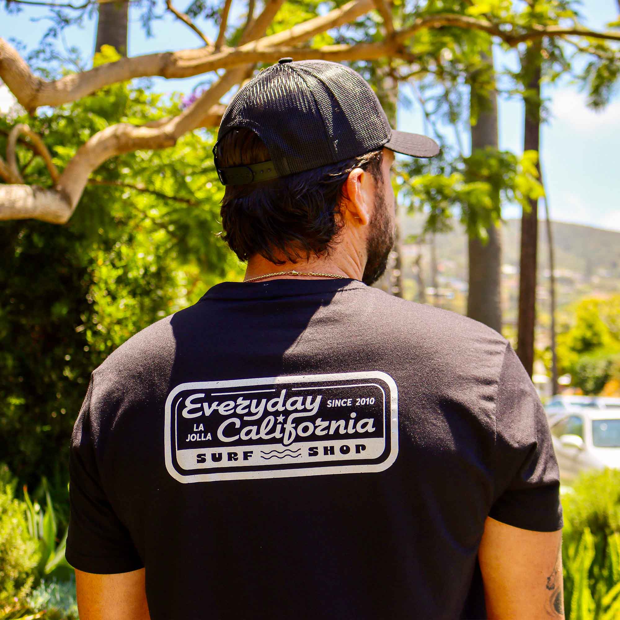 A model showcasing the Everyday California Surf Shop Tee logo on the back of the shirt
