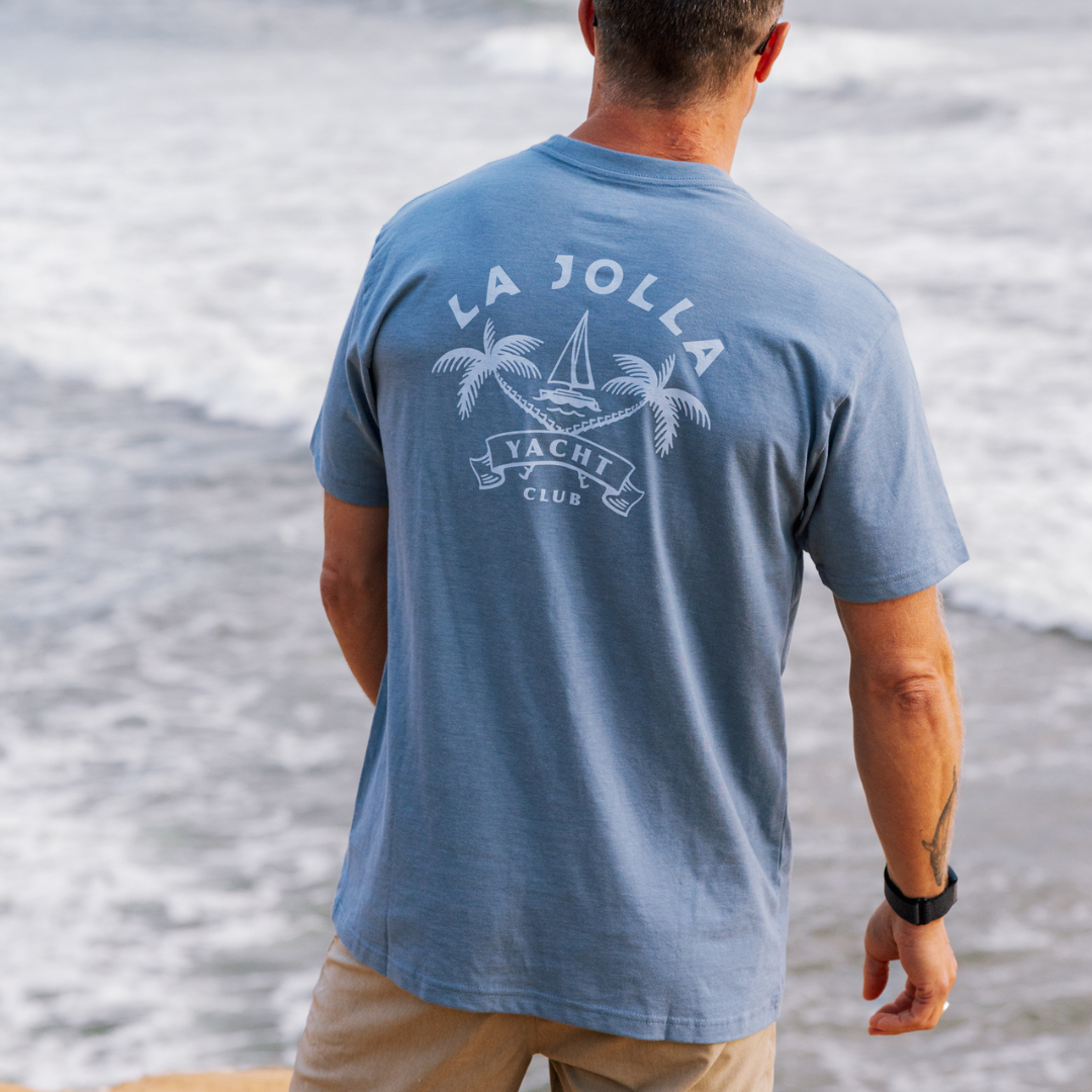 Man wearing a blue t-shirt with 'La Jolla Yacht Club' logo by the water.