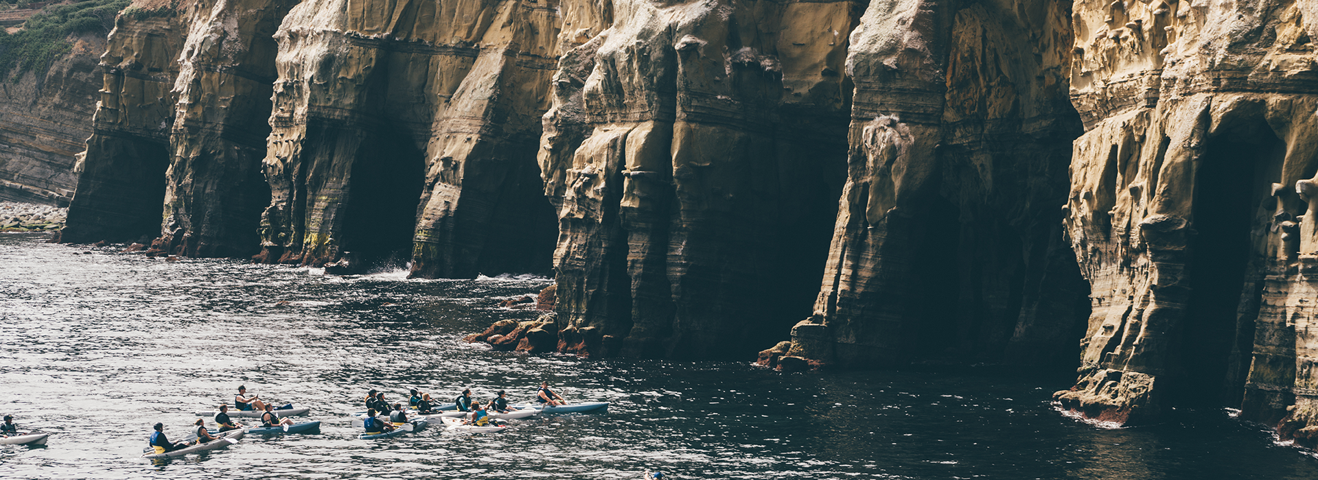 Image of the seven sea caves in La Jolla, California with a group of kayakers in the ocean at the mouth of the cave.