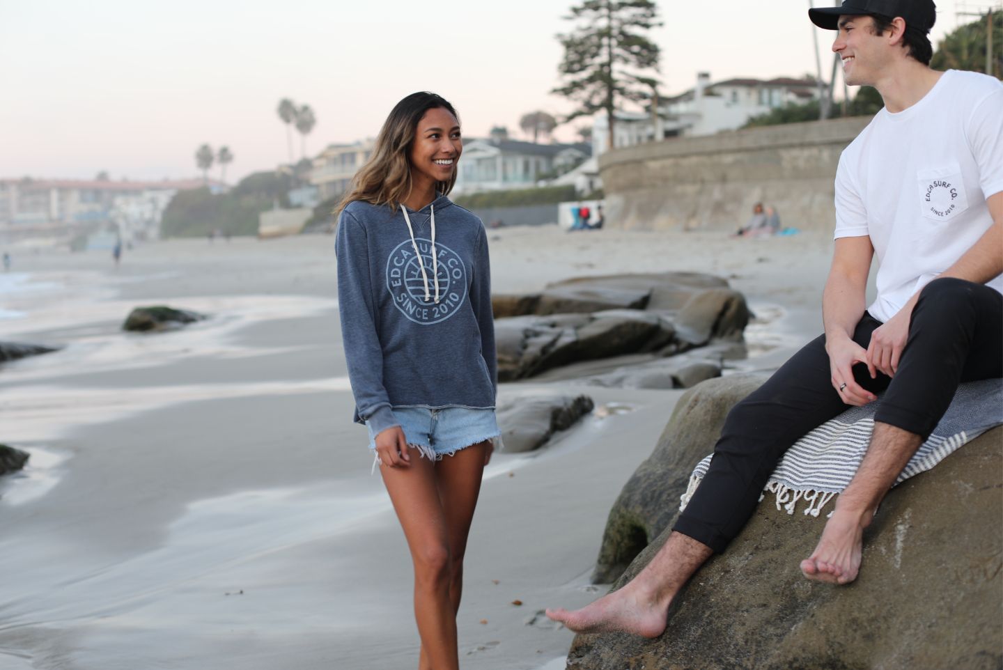 A boy and a girl talking on the beach with shoes off and very close to the water