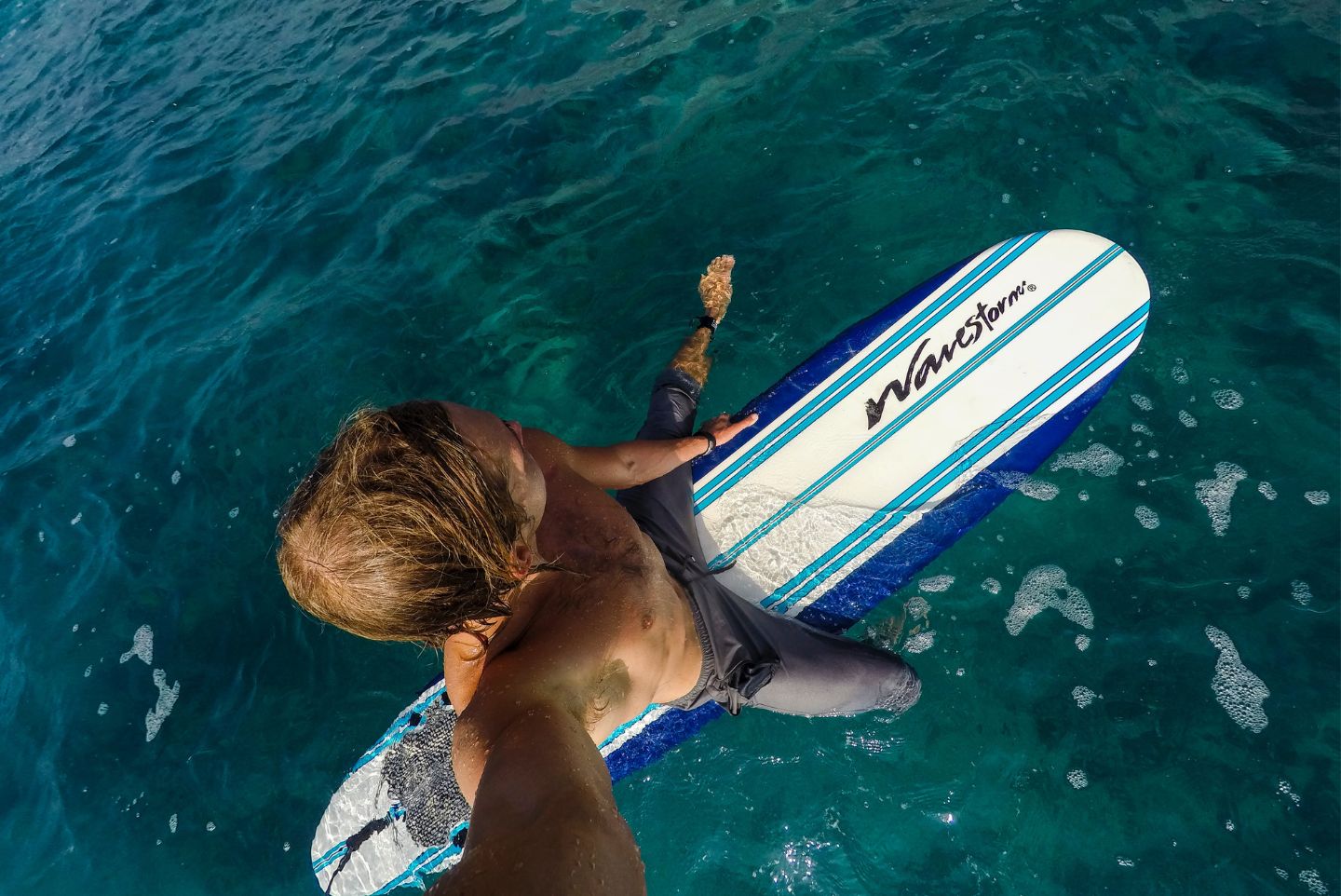 a surfer wearing his wetsuit half on taking a photo of himself in the water on a foam board