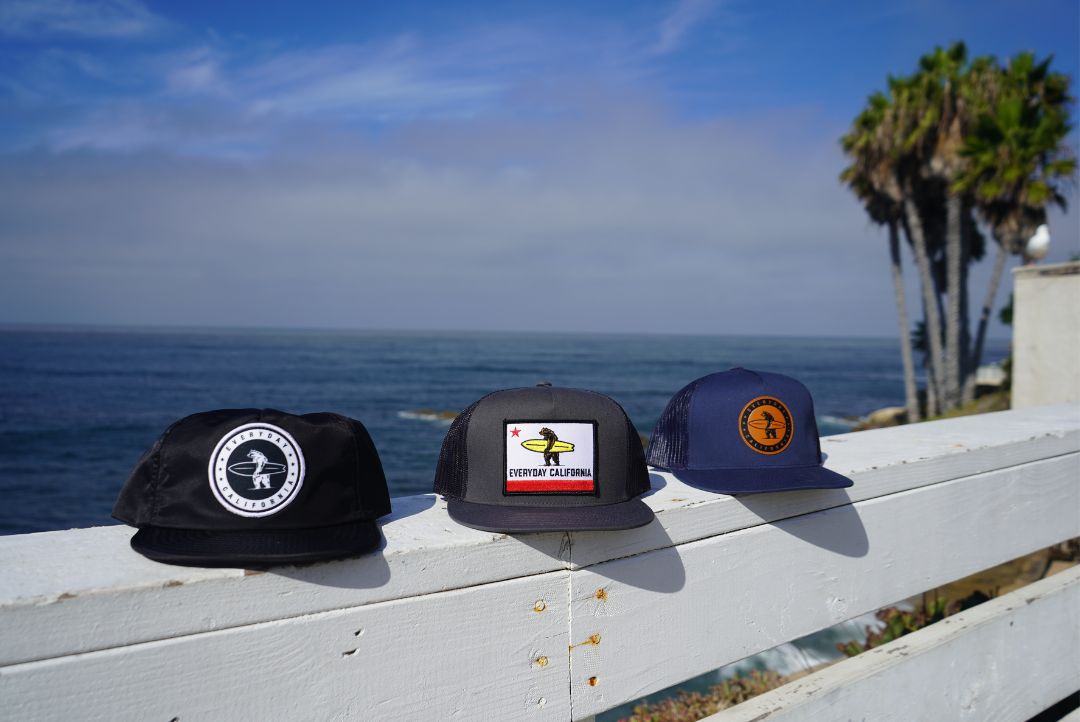a collection of everyday California hats in front of the beach