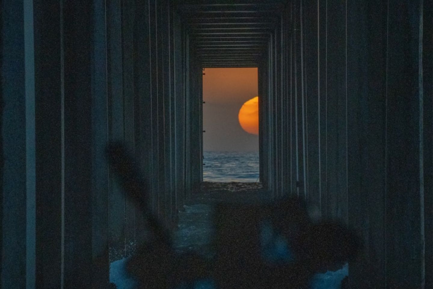 A sunset with the orange sun through silhouette of the bottom of the pier in La Jolla. 