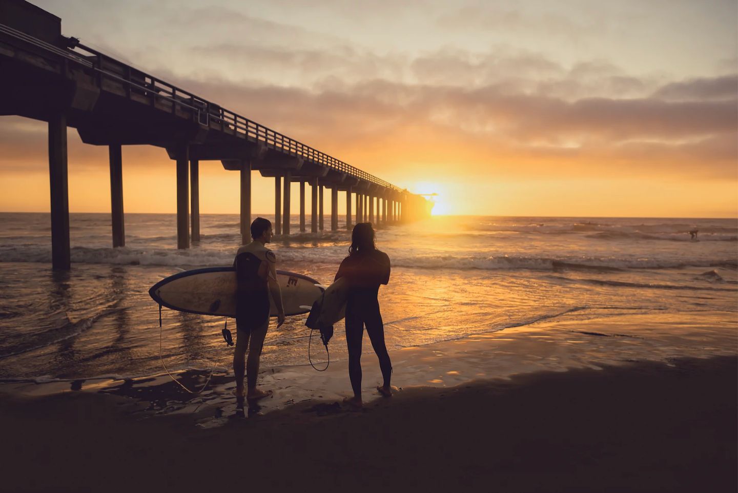 Silhouettes of two girls abut to go surf the Pacific Beach San Diego waves at sunset