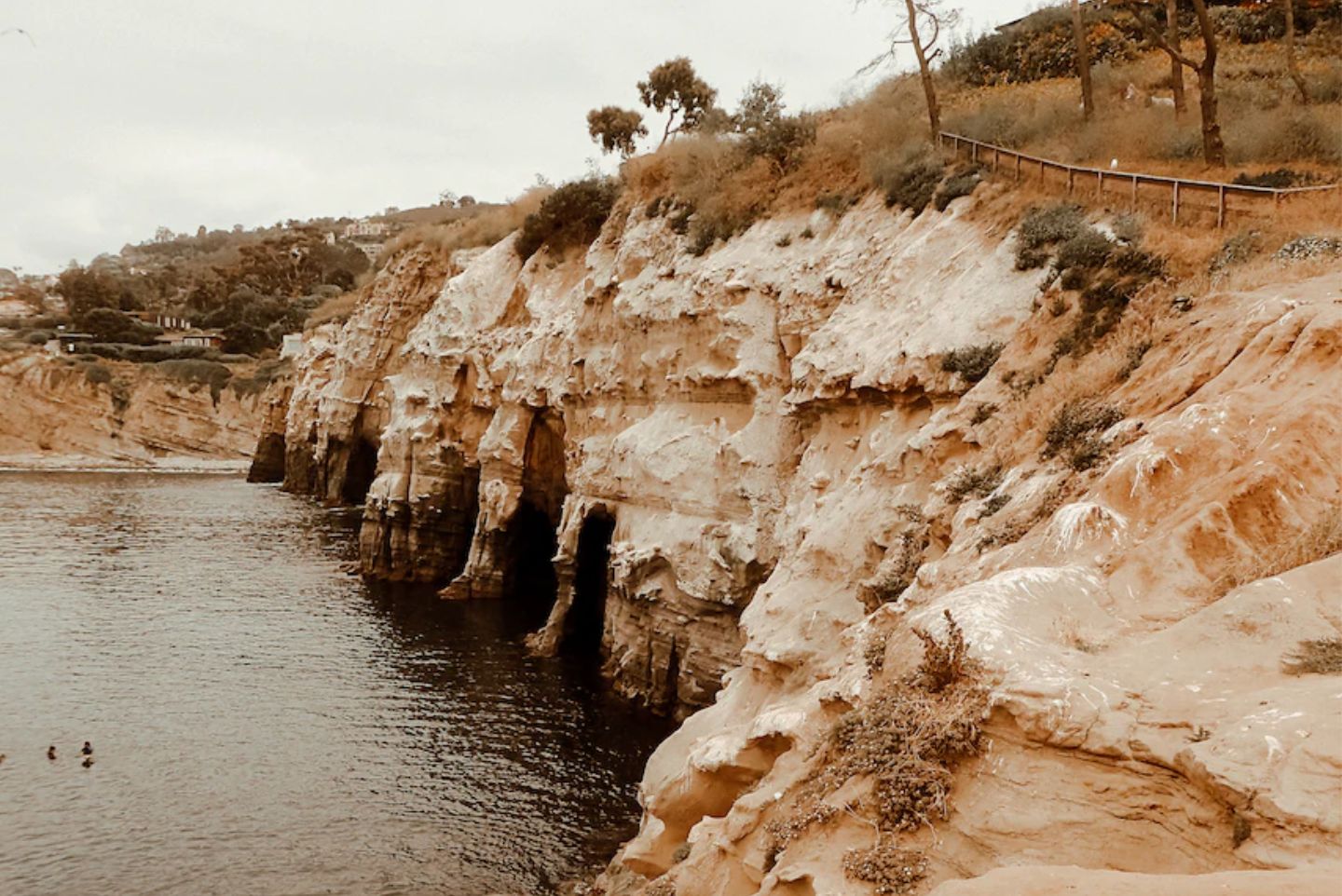 Side view of the La Jolla Seven Sea Caves and the water is calm with looming sandy cliffs. 