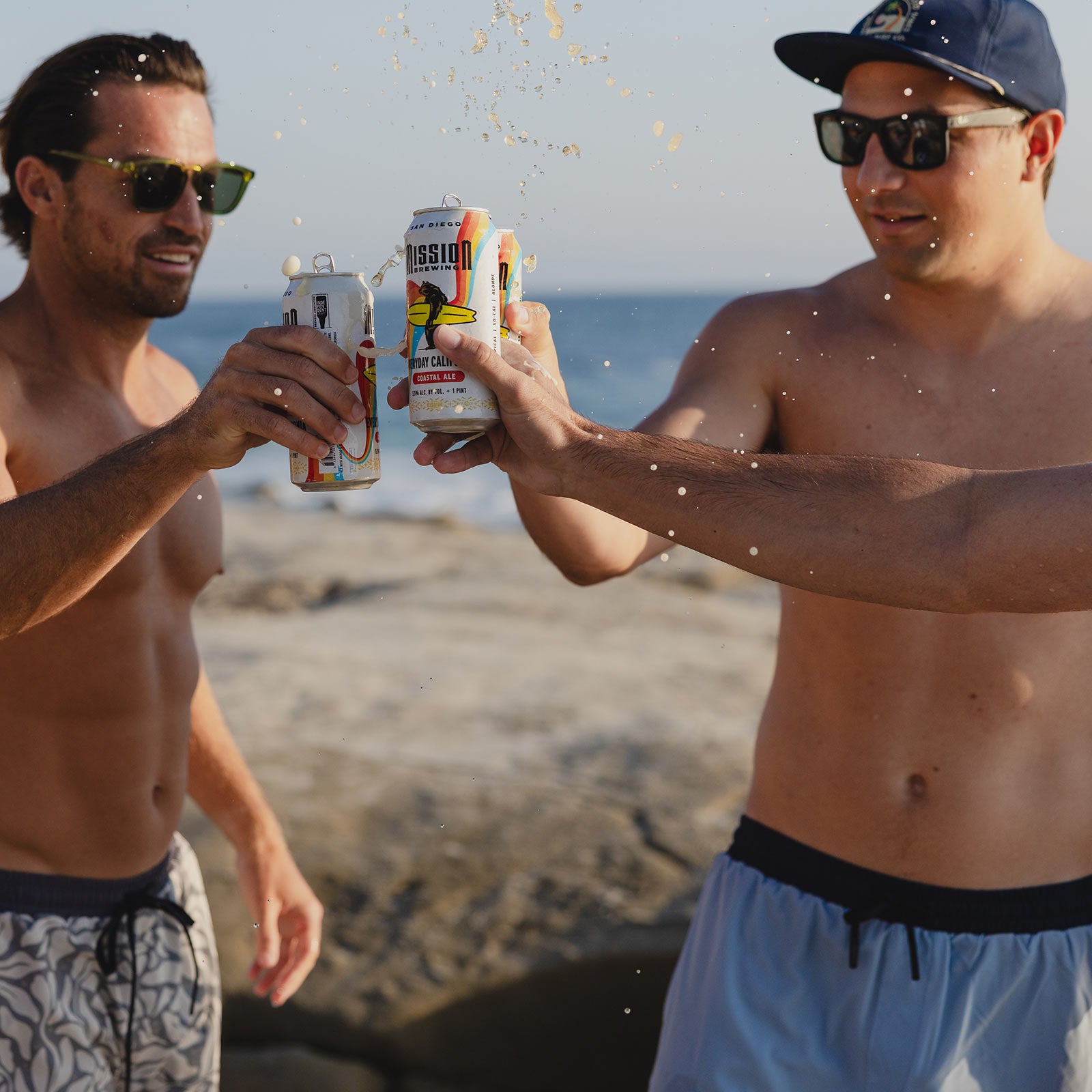 Man wearing Everyday California light blue board shorts with navy trim drinking with friends on the beach