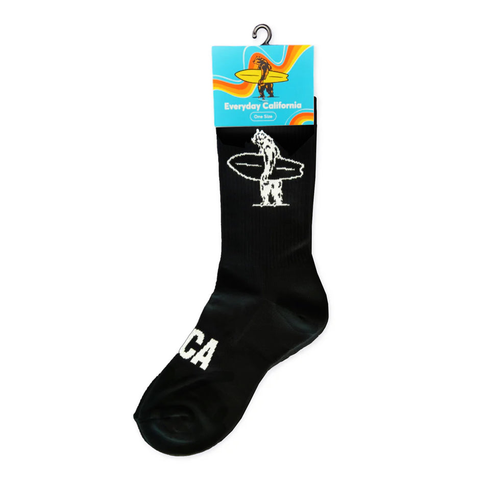Black athletic socks with white logos on them that say "EDCA" across the top of the foot and a bear holding a surfboard on the inner and outer calf of the sock.