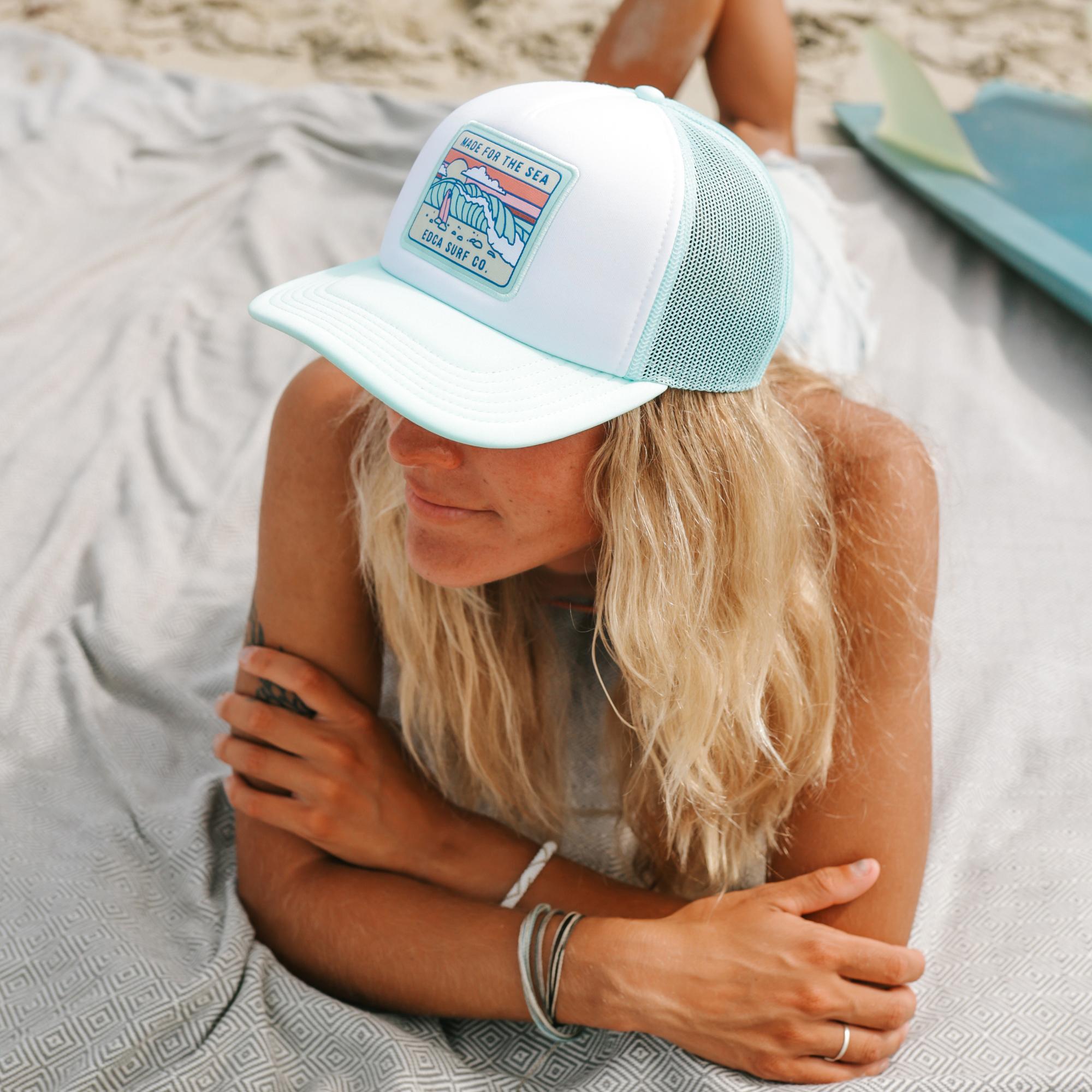 Woman wearing a cap with an Everyday California hat on sitting on a blanket outdoors.