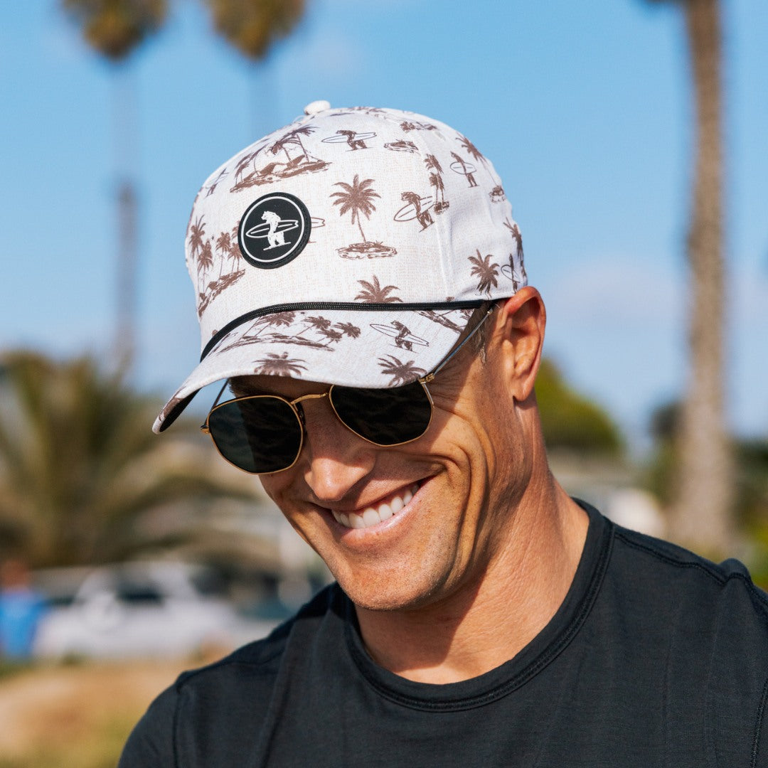 Man wearing a patterned Coastal Division Hat and sunglasses with palm trees, outdoors.