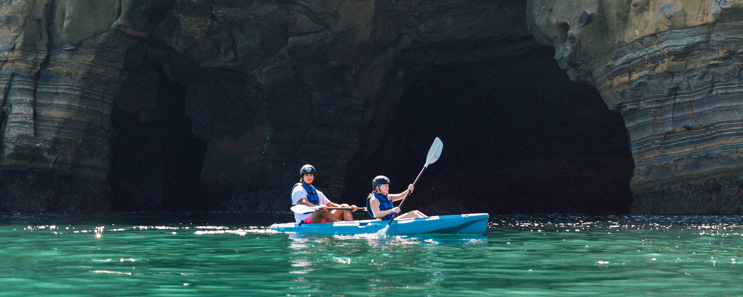 Two kayakers on a Kayaking Tour with Everyday California, paddling their kayak in front of the entrance of a sea cave in La Jolla.